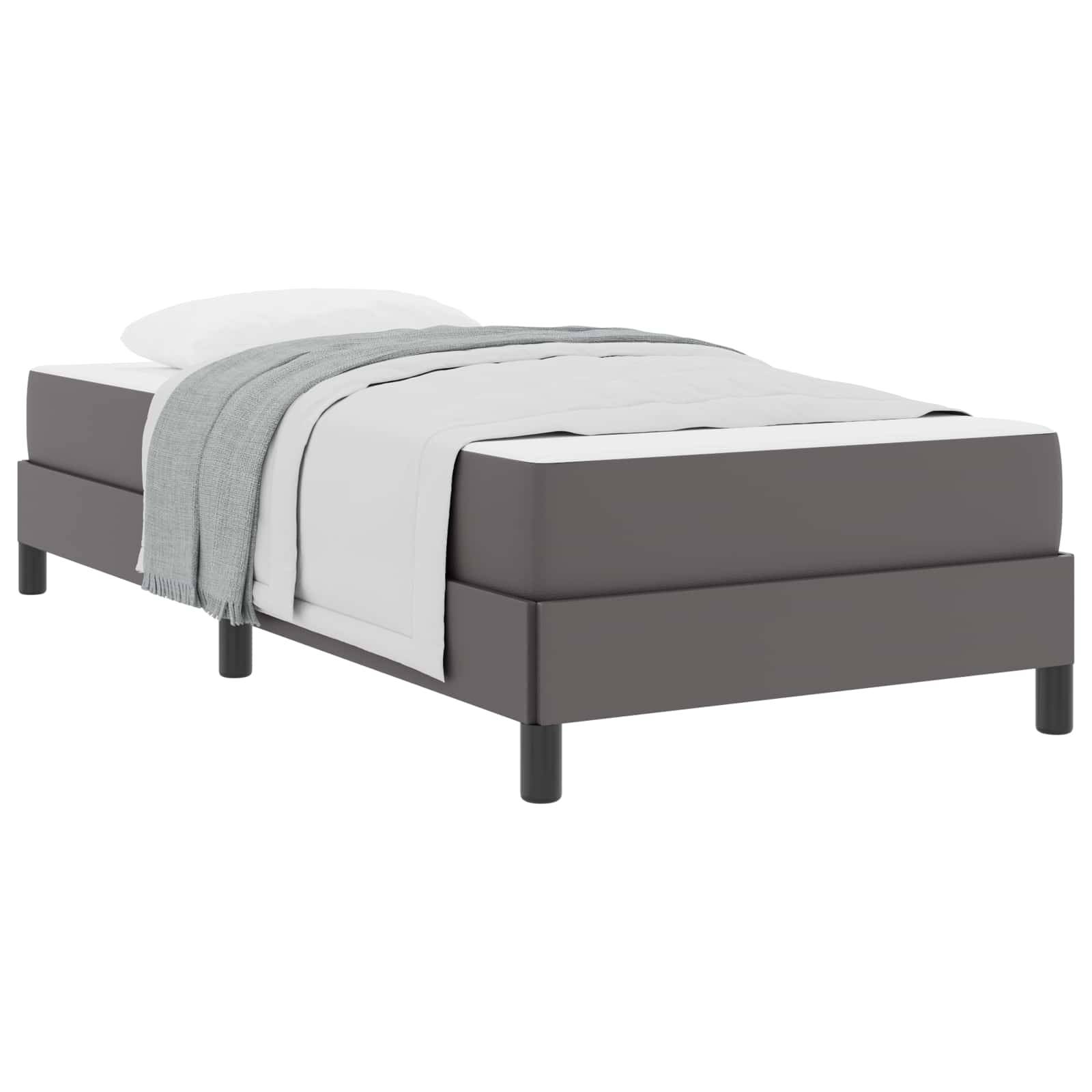 Ein Einzelbett mit einer grauen Basis, weißer Bettwäsche, einem weißen Kissen und einer ordentlich drapierter grauer Decke darüber.
