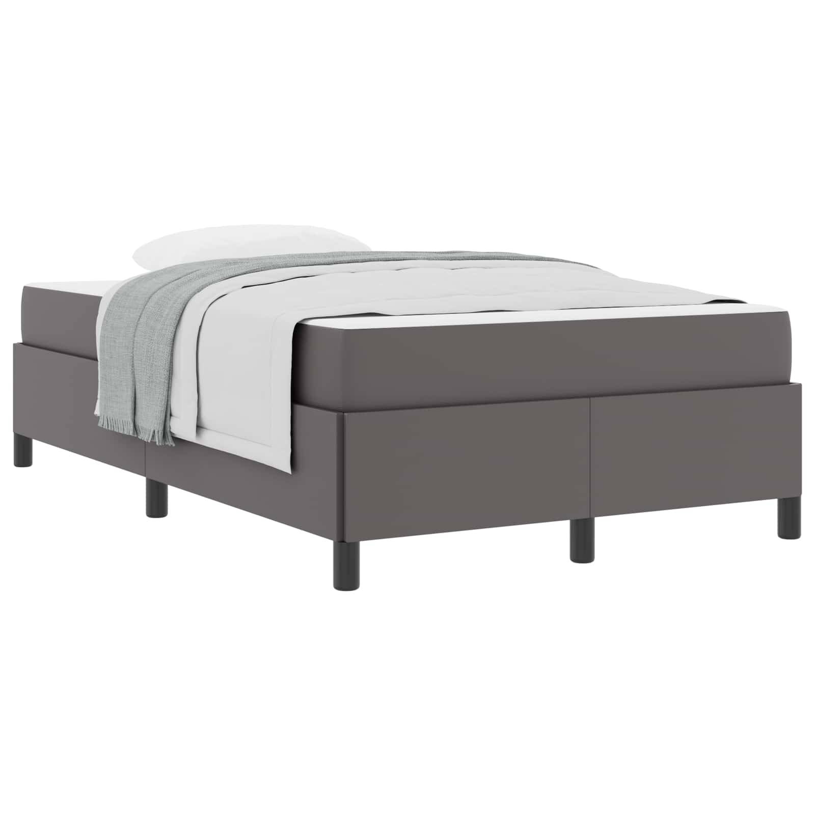Grau gepolstertes Bett mit weißer Bettwäsche und einer gefalteten Wurfdecke, gezeigt vor einem einfachen weißen Hintergrund.