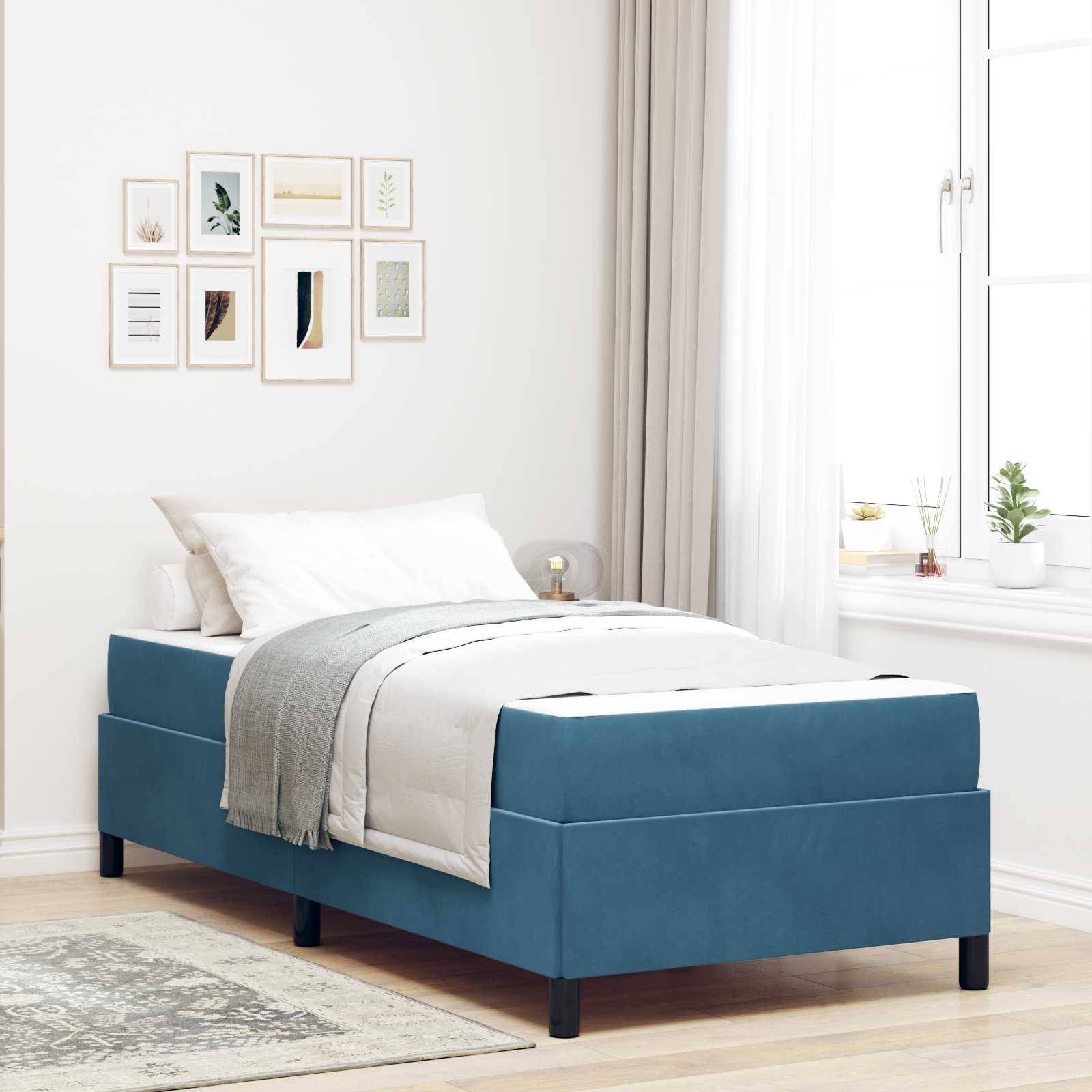 Ein ordentlich gemachtes Bett mit blauem Rahmen und weißer Bettwäsche steht in einem hellen, minimalistischen Schlafzimmer. Mehrere gerahmte Kunstwerke hängen über dem Bett.