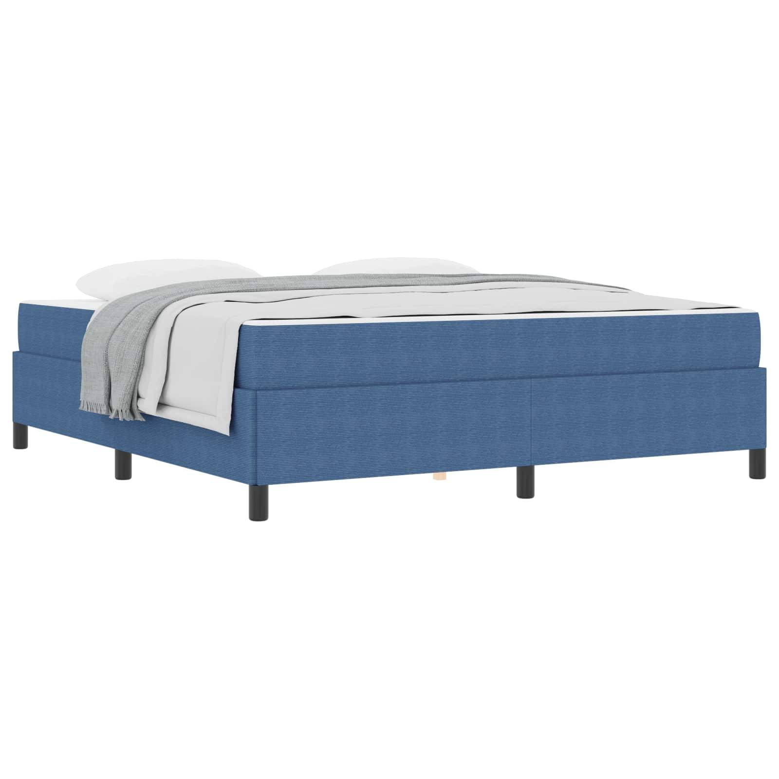 Ein modernes Bett mit blauer Polsterung und schwarzen Beinen, ordentlich bezogen mit weißen Kissen und einer grauen Decke, die seitlich herunterhängt.