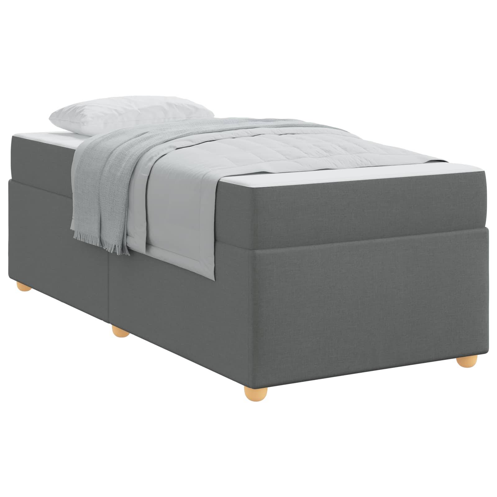 Ein graues gepolstertes Einzelbett mit einem weißen Kissen und einer Decke, in einem modernen und minimalistischen Design, auf kleinen Holzbeinen stehend.