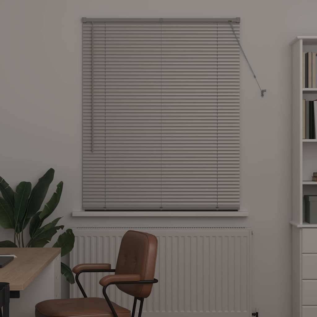 Ein kleines Büro mit einem Schreibtisch, einem Stuhl und einem Bücherregal. Eine Pflanze steht neben dem Fenster, und Jalousien bedecken das Fenster über einem Heizkörper.