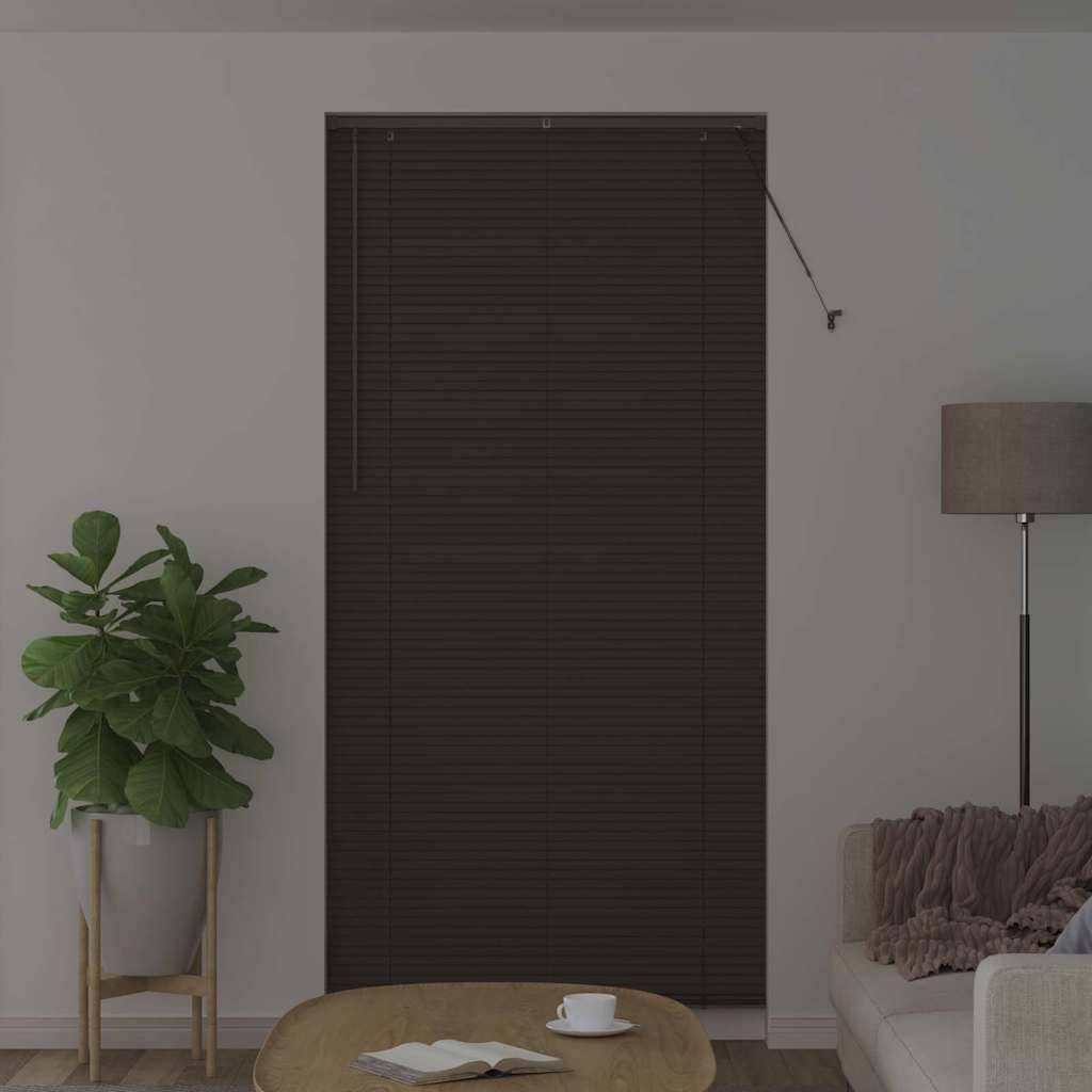 Ein Wohnzimmer mit geschlossenen dunklen Jalousien, einer Stehlampe, einer Topfpflanze und einem runden Holztisch mit einer weißen Tasse.