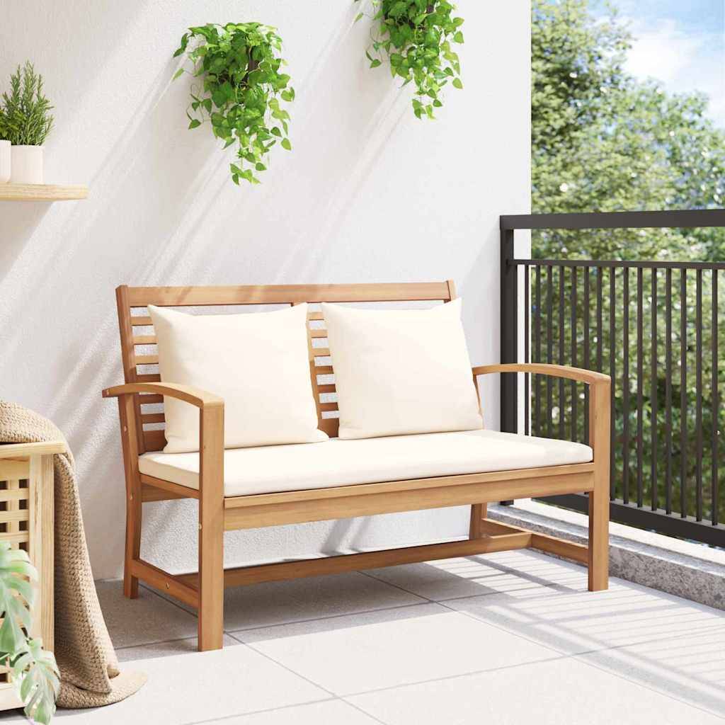 Holzbank mit weißen Kissen auf einem Balkon, umgeben von grünen Pflanzen, unter einem klaren Himmel.
