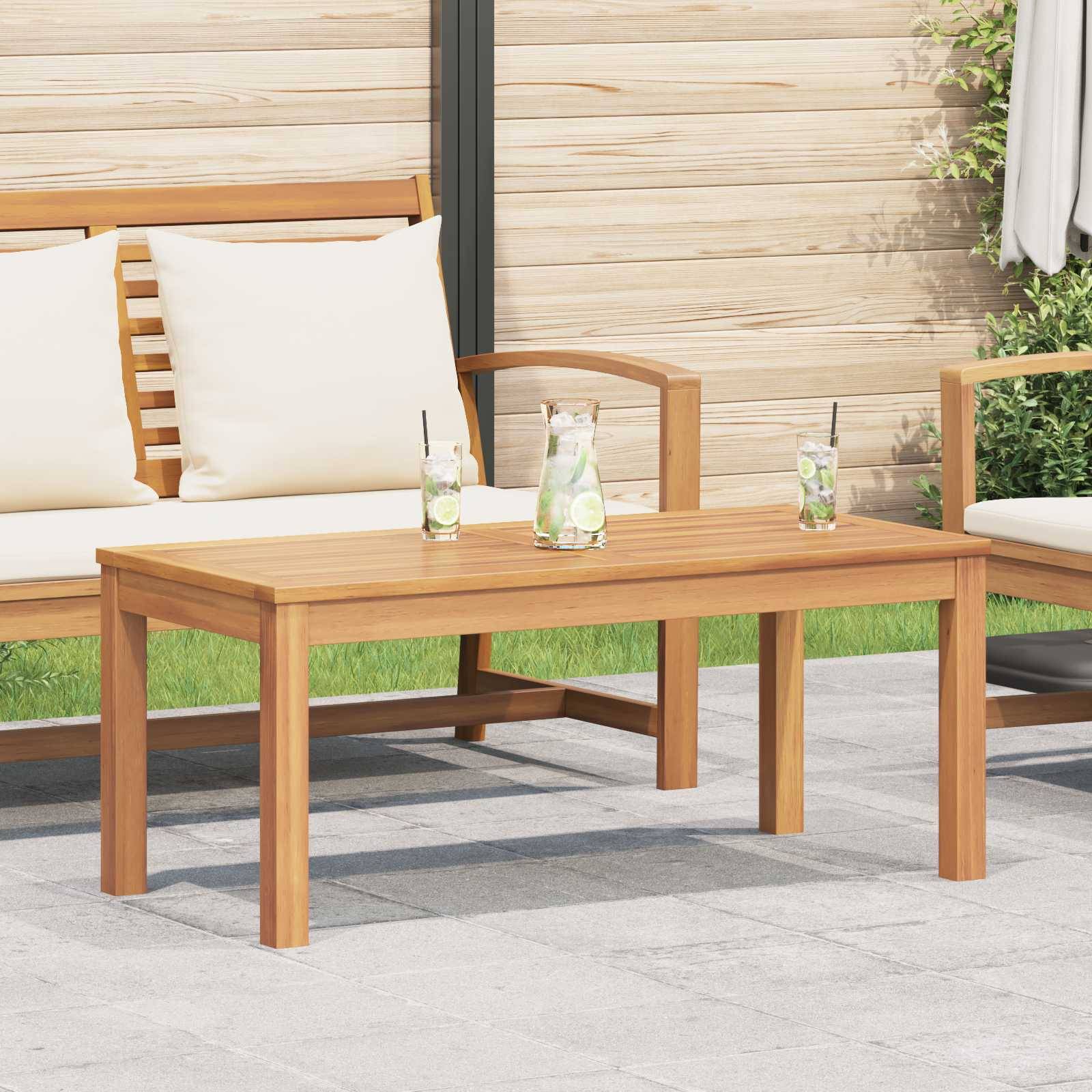 Eine Terrassenmöblierung mit einem Holztisch und Stühlen, die weiße Kissen aufweisen. Zwei Gläser mit Zitronenscheiben stehen auf dem Tisch.