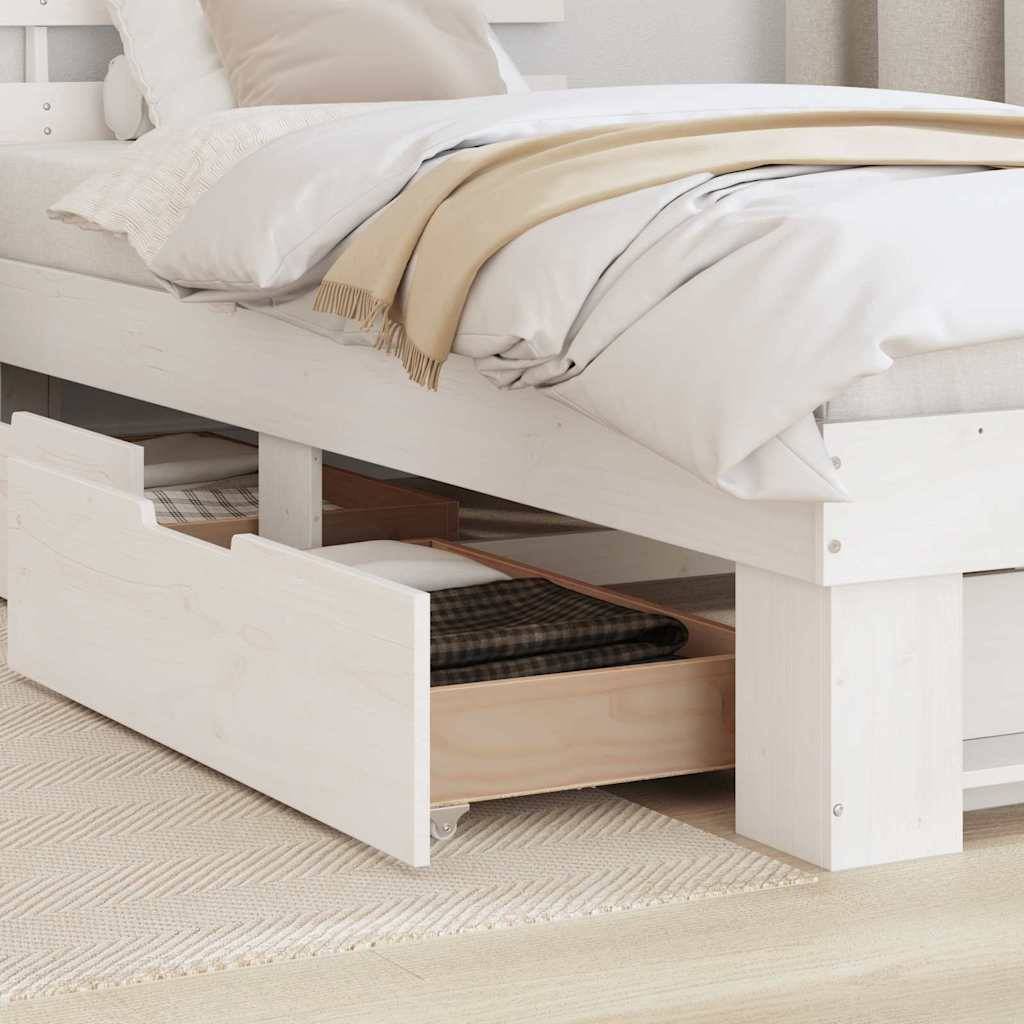 Ein ordentlich gemachtes Bett mit weißen Leintüchern und beigen Decken, wobei eine offene Schublade unter dem Bett eine gemusterte Decke und ein Buch enthält.