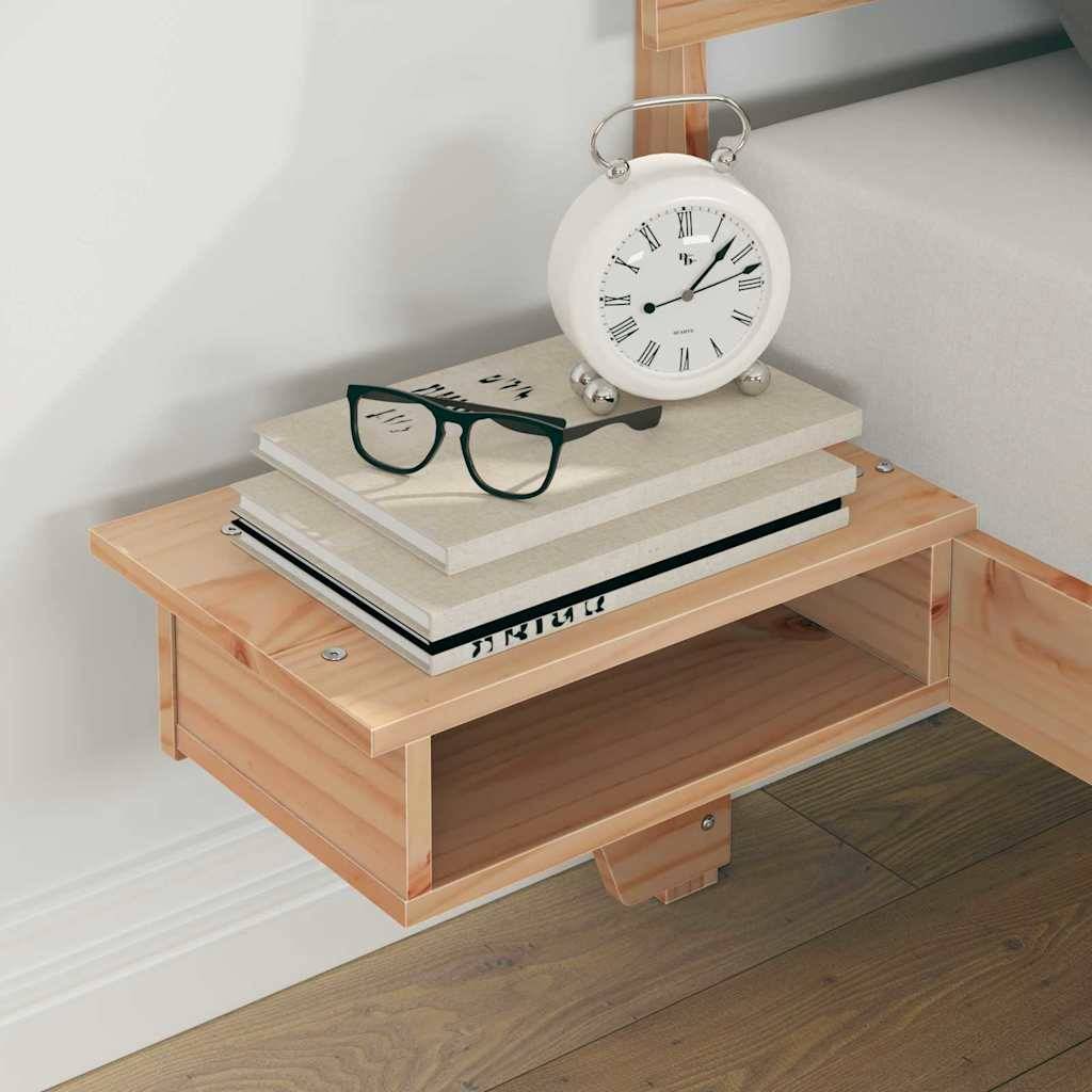 Ein Holznachttisch trägt einen weißen Wecker, einen Stapel Bücher und eine Brille mit schwarzem Rand, vor einer hellgefärbten Wand.