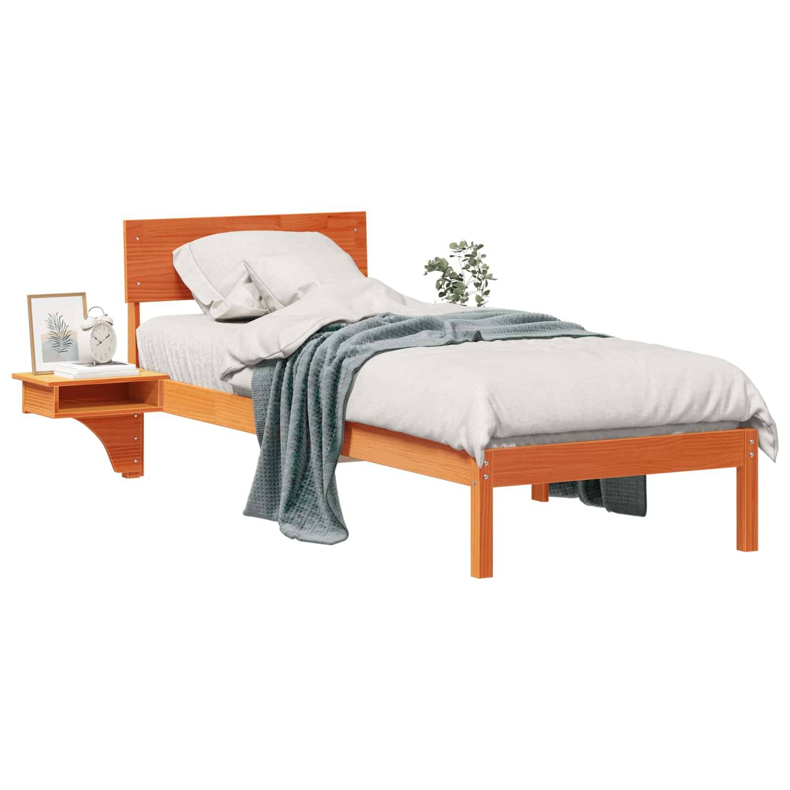 Ein Holz-Einzelbett mit weißer Bettwäsche und einer grauen Decke, die darüber drapiert ist. Ein kleines Regalbrett daneben trägt Bücher und ein gerahmtes Bild.