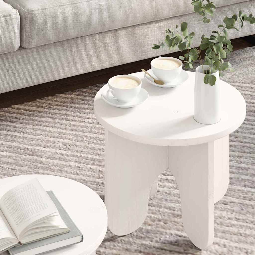 Zwei kleine runde weiße Tische auf einem Teppich; einer trägt ein aufgeschlagenes Buch, der andere zwei Kaffeetassen und eine Vase mit Grünpflanzen. Beige Sofa im Hintergrund.