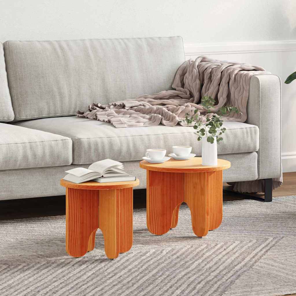 Ein gemütliches Wohnzimmer mit einem grauen Sofa, einer drappierten Decke und zwei Holztischen. Auf jedem Tisch liegt ein Buch, steht eine Pflanze und eine Tasse Kaffee.