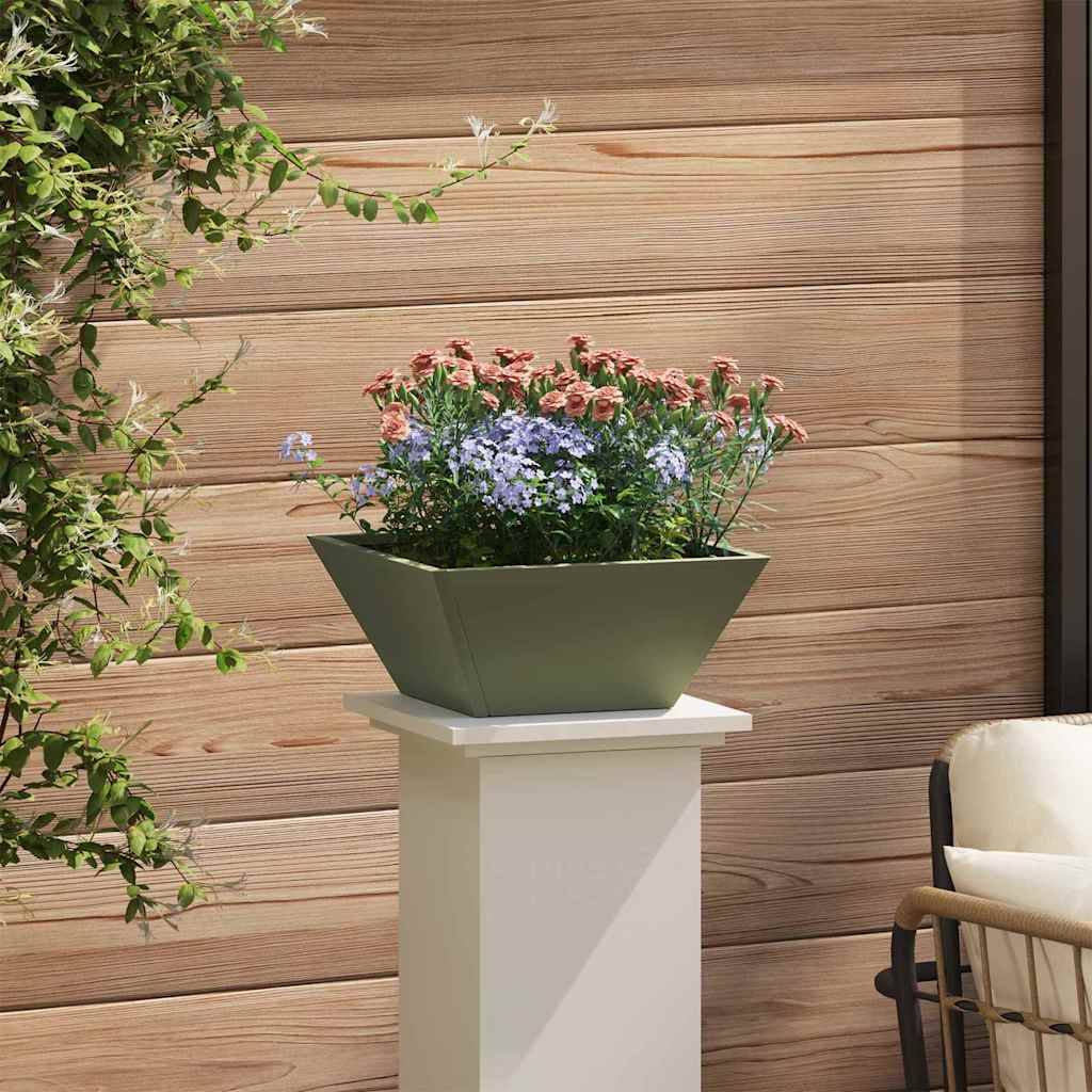 Ein grüner Blumentopf mit rosa und blauen Blumen steht auf einem weißen Podest an einer Holzwand, neben einem weißen gepolsterten Stuhl und einer blattreichen Pflanze.