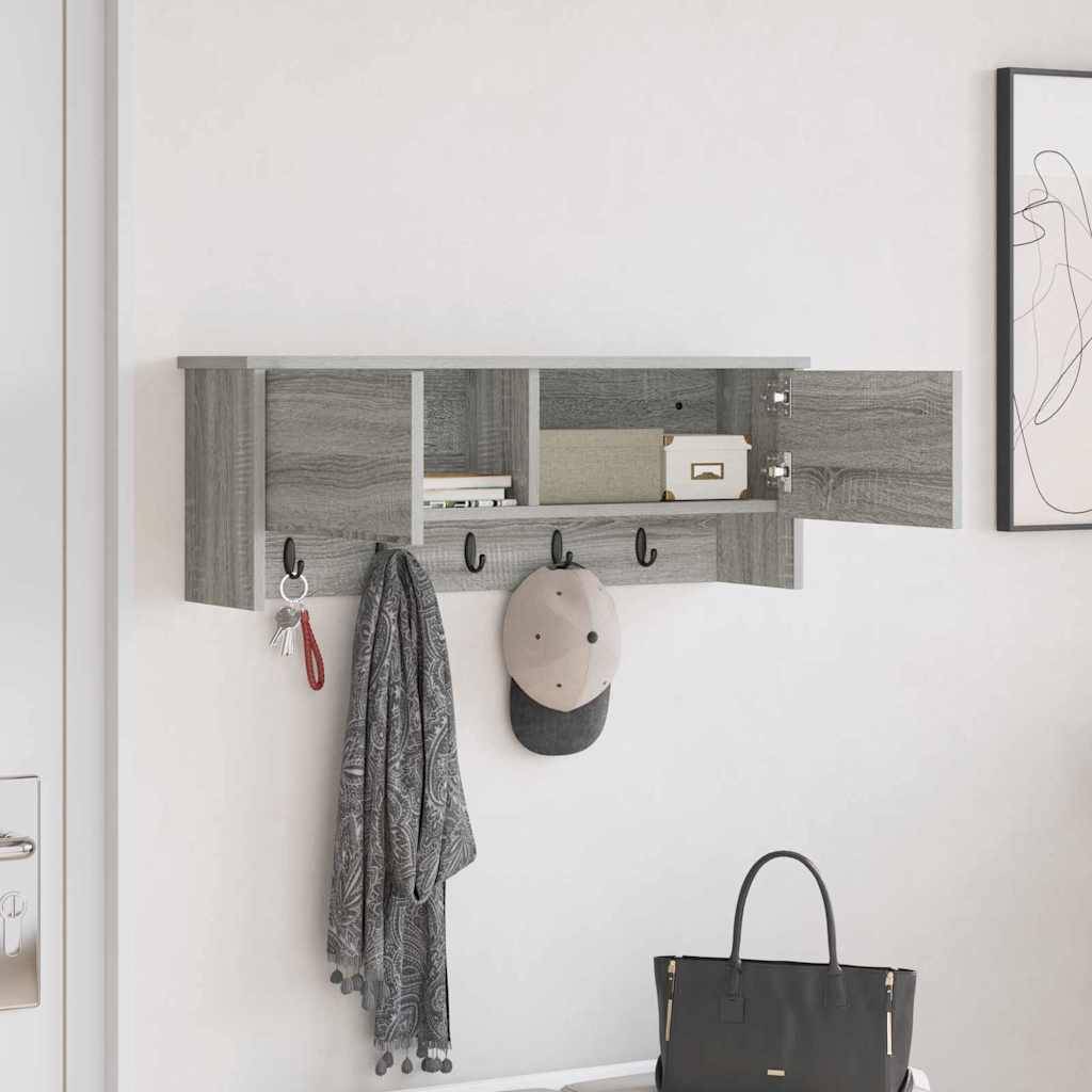 An der Wand montiertes graues Regal mit Haken, an denen ein Mantel, ein Hut und eine Tasche hängen. Die Regale enthalten Bücher und Dekorationsgegenstände. Eine Tür und Kunstwerke sind teilweise sichtbar.