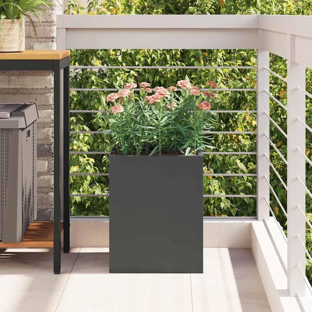Ein moderner Balkon mit einem Holztisch, einem kleinen Grill darunter und einem großen grauen Pflanzgefäß, gefüllt mit rosa Blumen, vor einem laubreichen Hintergrund.