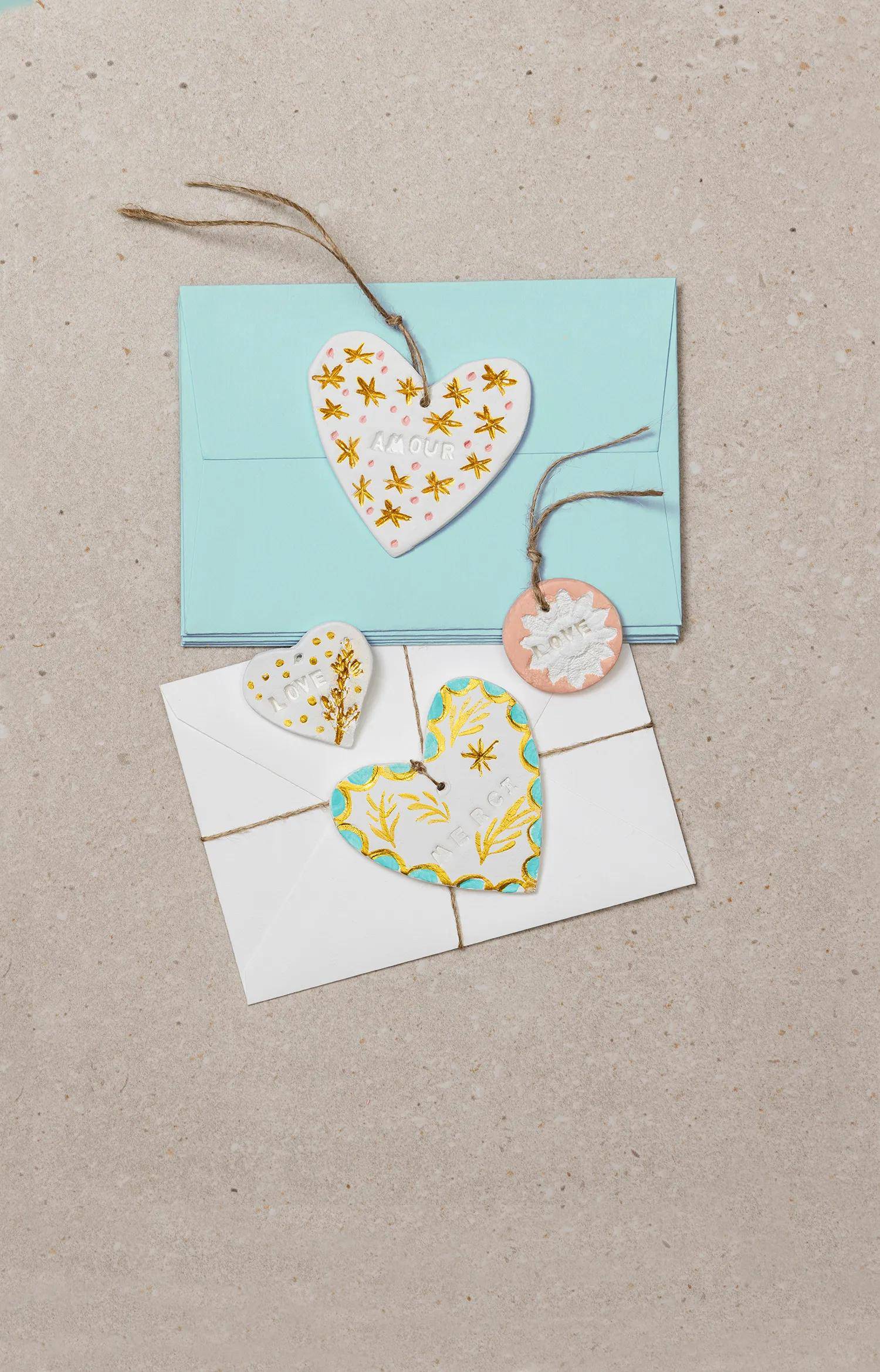 Zwei dekorierte Geschenkumschläge mit herzförmigen Anhängern oder Karten auf einer neutralen Oberfläche, einer in Aquamarin und einer in Weiß, gebunden mit Schnur.