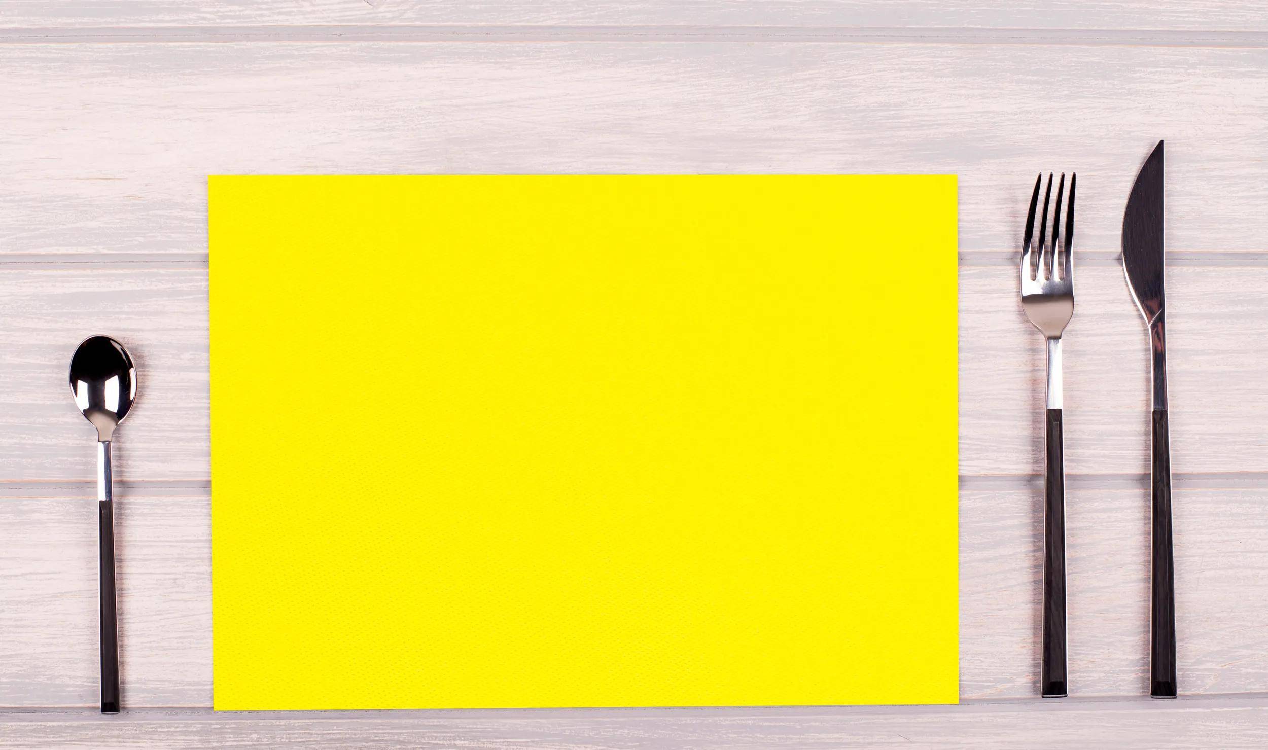 Ein leuchtend gelbes rechteckiges Papier auf einer hellen Holzoberfläche platziert.