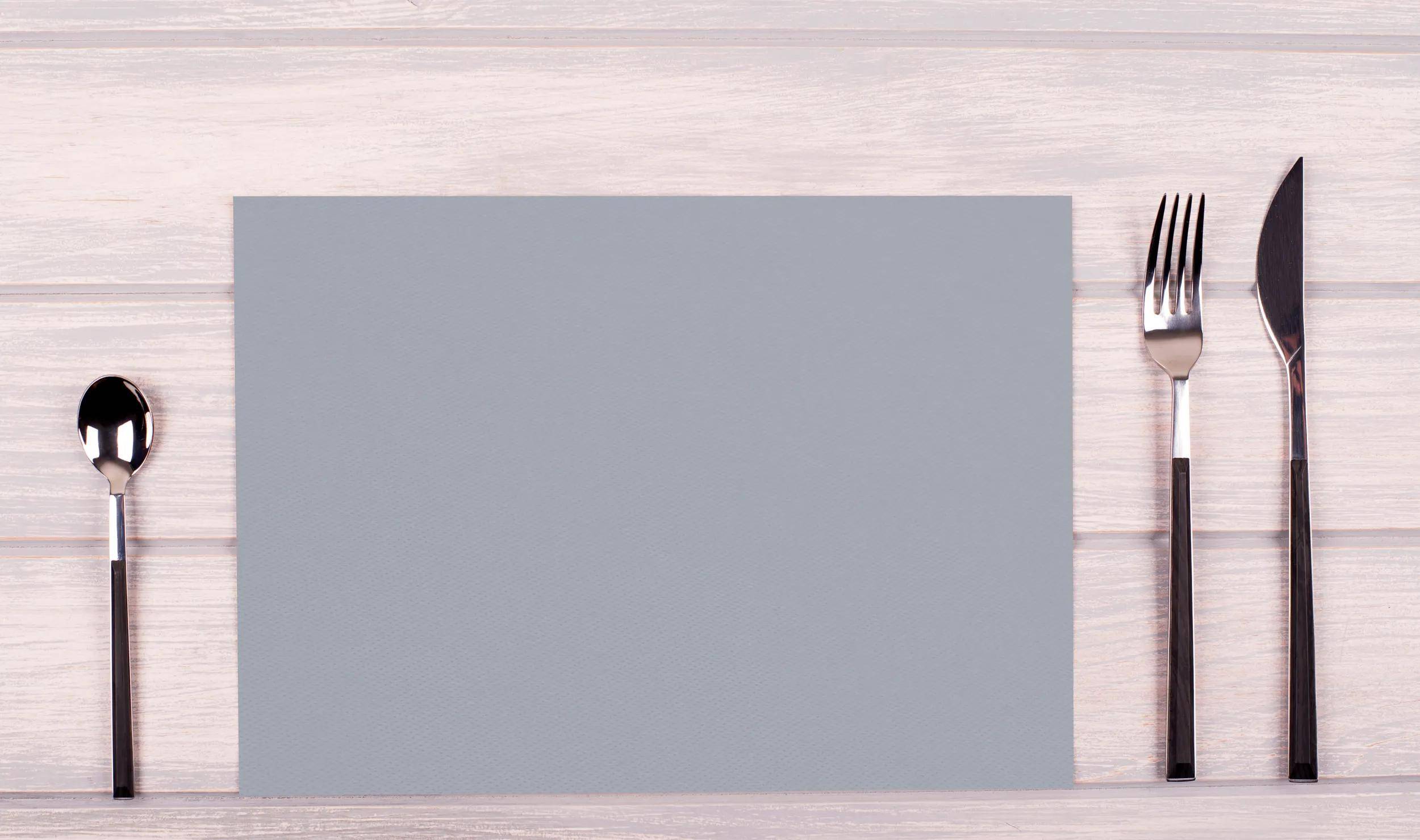 Ein grauer rechteckiger Platzdeckchen ist auf einem hellen Holztisch platziert und nimmt die Mitte des Bildes ein. Die umliegende Fläche ist uncluttered.
