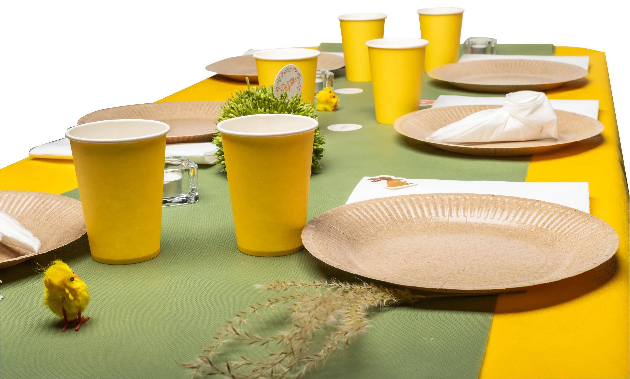 Eine Tischdecke mit gelben Tassen, braunen Tellern, einer grünen Tischdecke, kleinen Pflanzen und dekorativen Elementen, die ein umweltfreundliches Thema andeuten.
