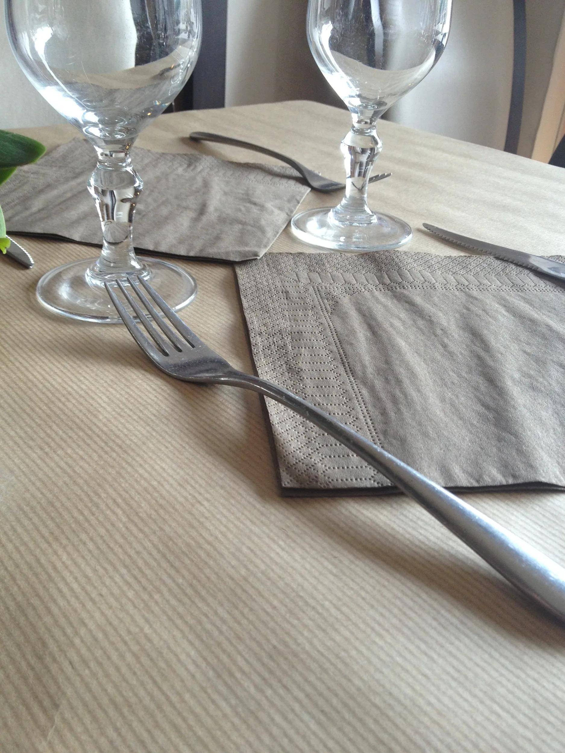 Ein Esstisch mit einer beigen Tischdecke, gefalteten Servietten, klaren Weingläsern und ordentlich angeordneten Gabeln, bereit für eine Mahlzeit.