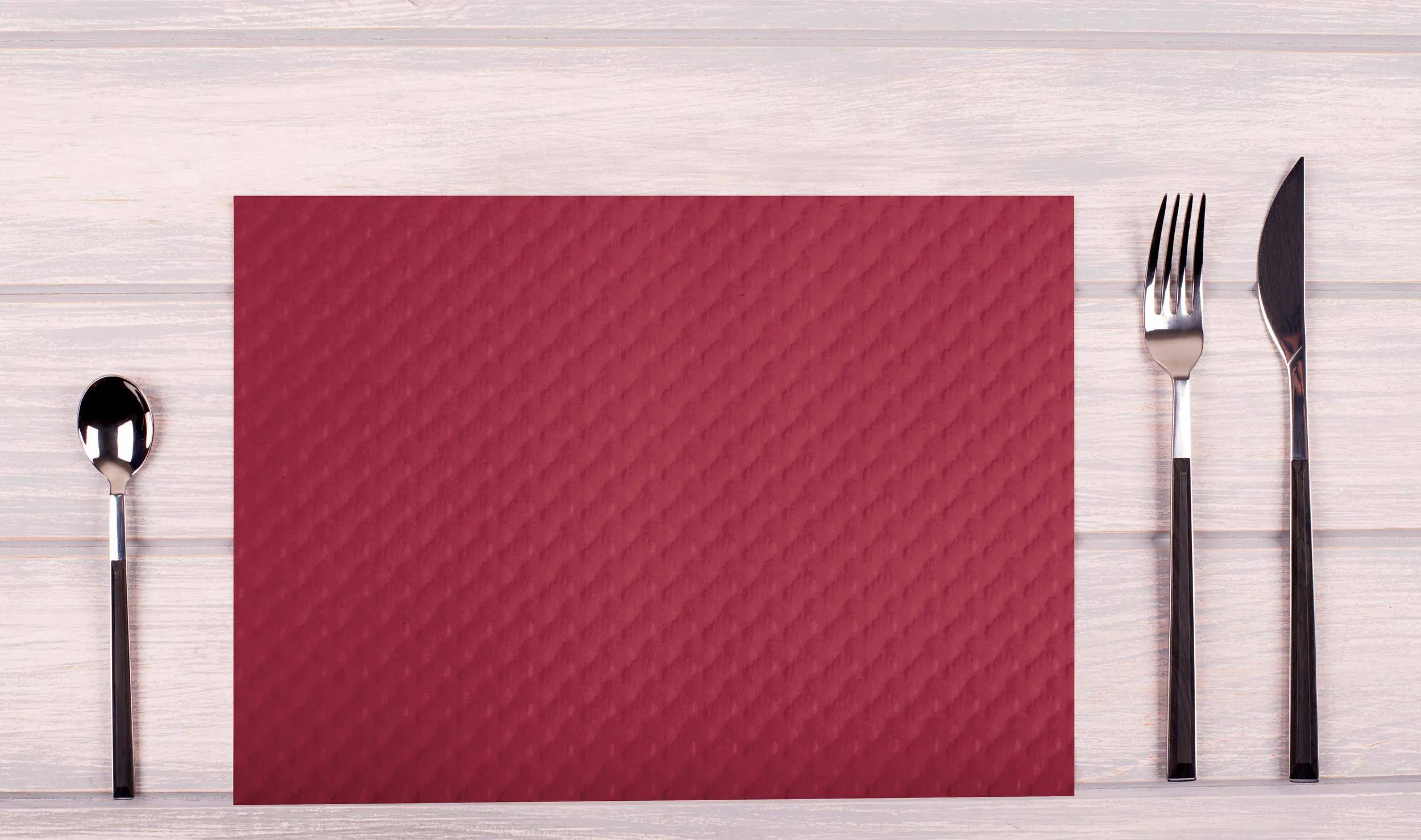 Eine rote strukturierte Matte liegt auf einer hellen Holzoberfläche und zeigt ein diagonales Muster aus kleinen, erhabenen Rautenformen.