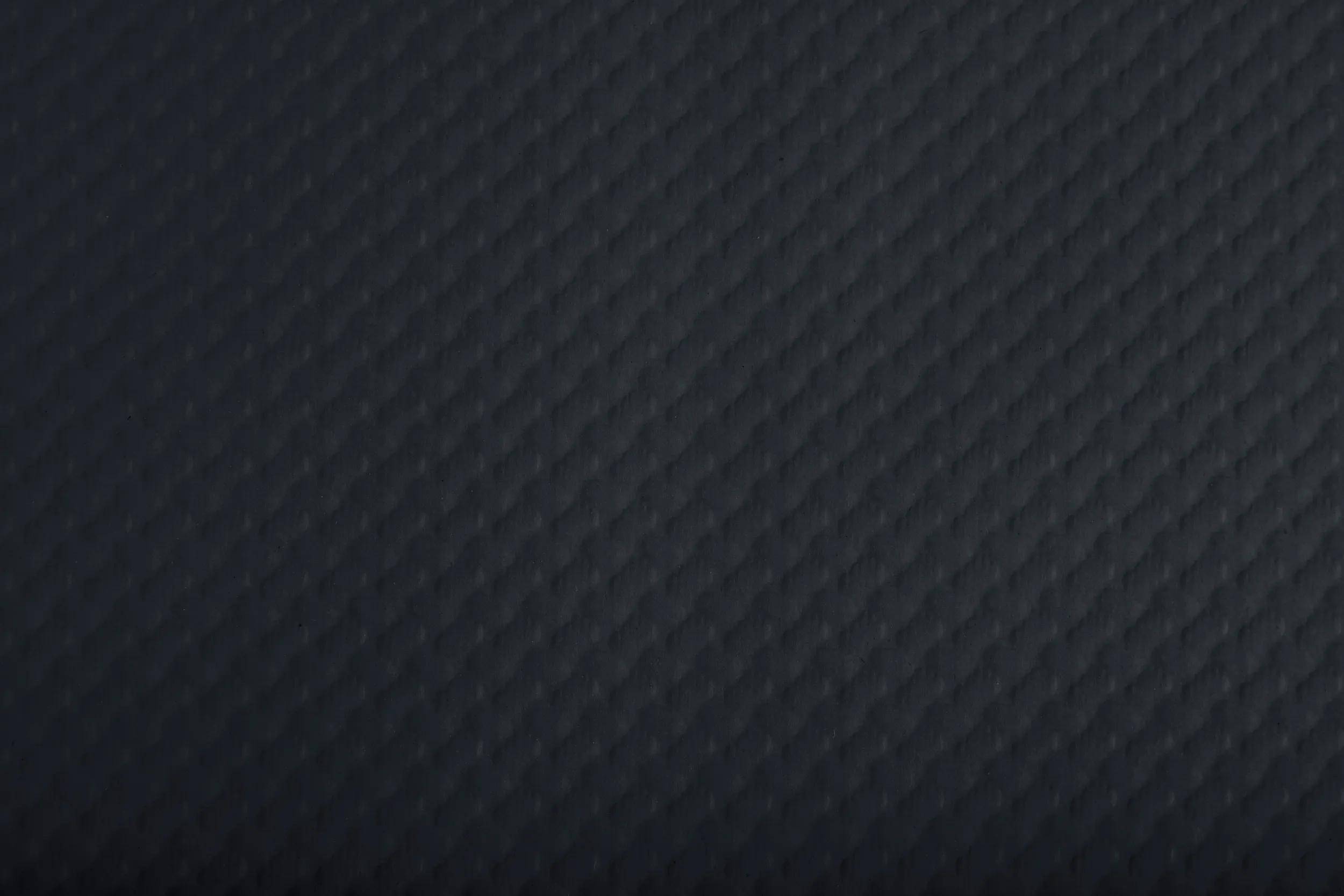 Eine strukturierte dunkle Oberfläche mit einem subtilen Rautenmuster, die einen Hintergrund mit einem eleganten und modernen Aussehen bietet.