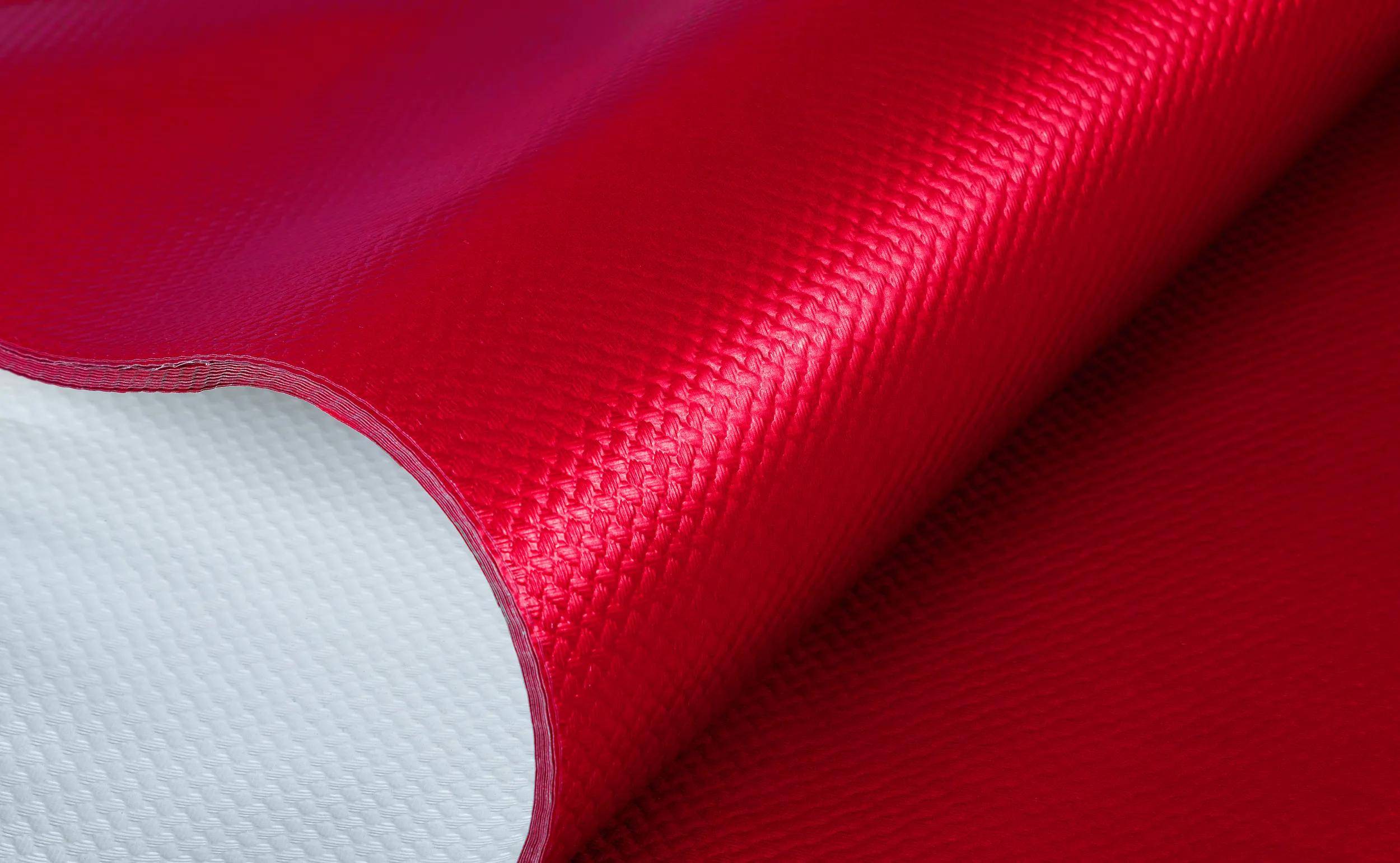 Ein rotes, strukturiertes Stoff- oder Materialblatt, das teilweise aufgerollt ist, um eine weiße innere Schicht zu enthüllen, was auf Haltbarkeit und Flexibilität hindeutet.