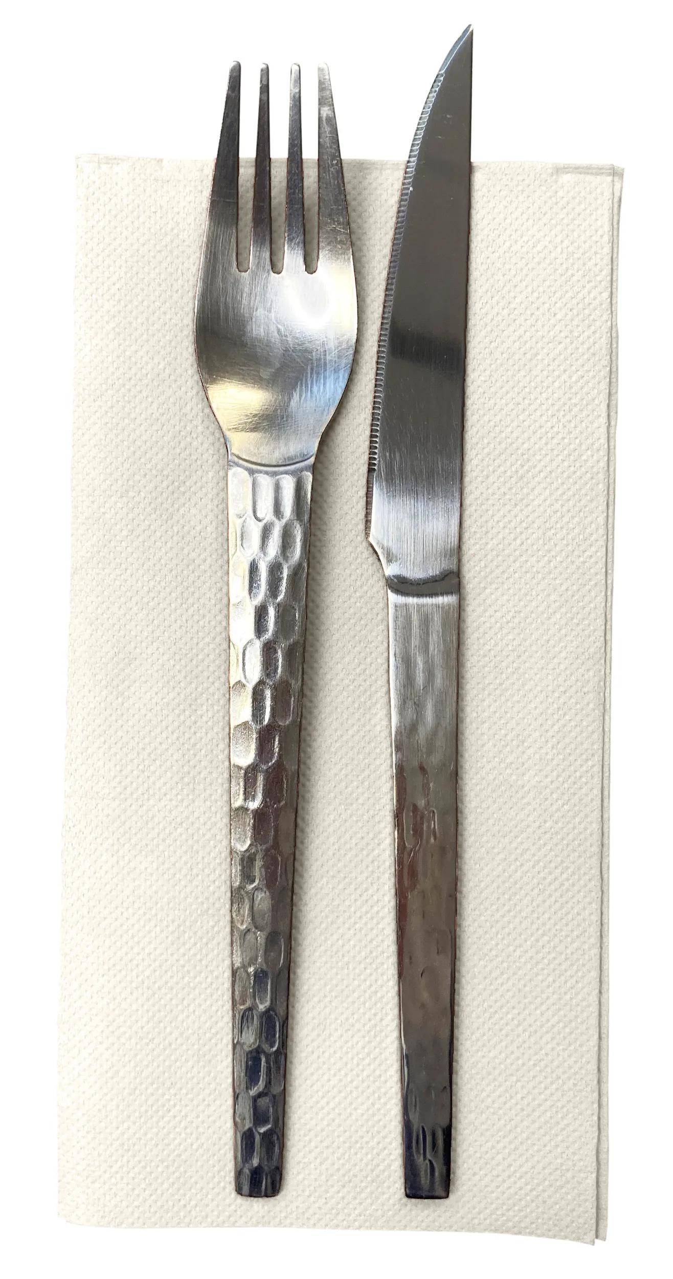 Ein Löffel und ein Messer mit einem strukturierten Metallgriff liegen auf einer weißen Serviette, von oben betrachtet.