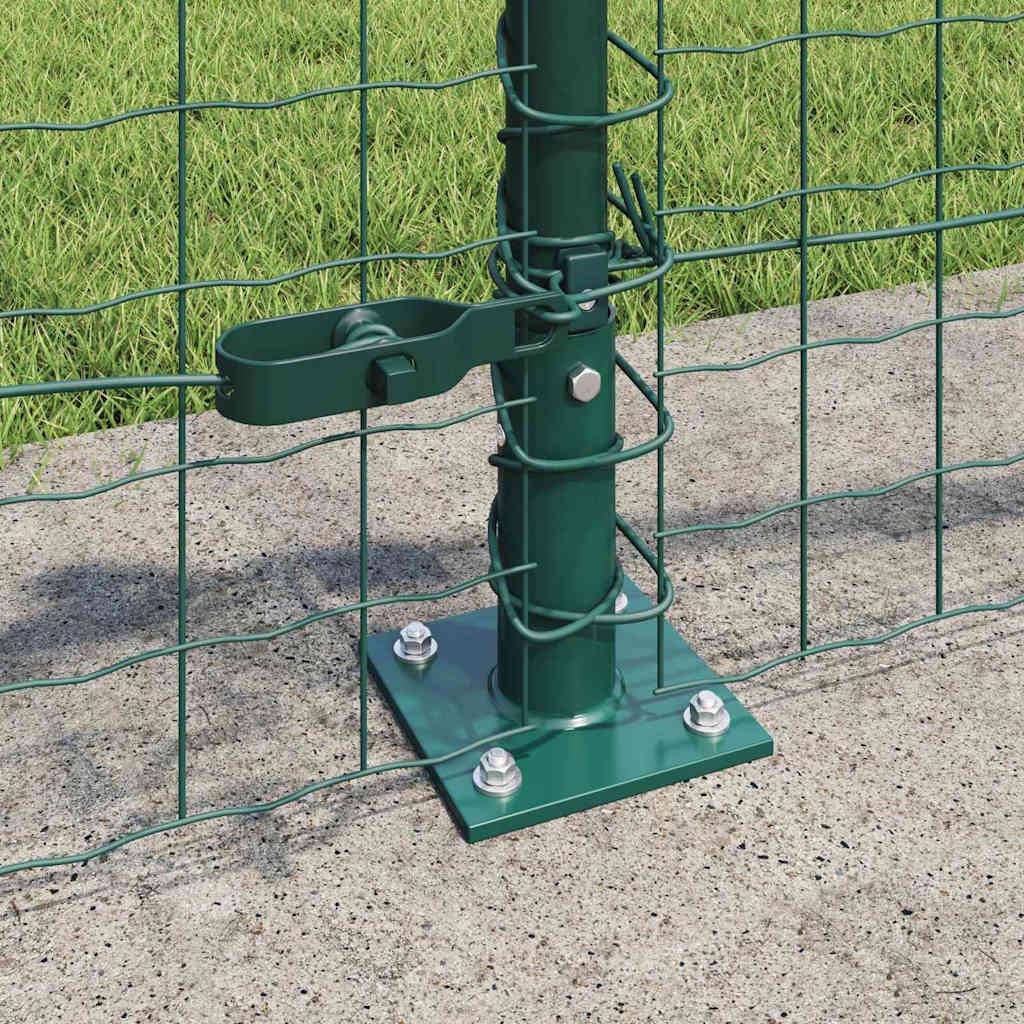 Ein grüner Metallzaunpfosten mit einem Maschendrahtzaun ist durch eine Metallbasisplatte mit Schrauben an einer Betonoberfläche befestigt. Gras ist sichtbar.