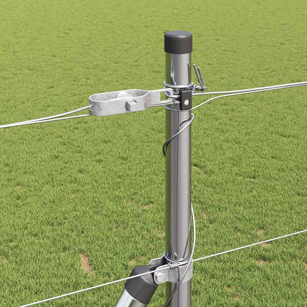 Ein Metallzaunpfosten, der im Gras verankert ist, trägt mehrere straff gespannte Drahtstränge, die mit Halterungen und Isolatoren befestigt sind, vor einem grünen Feldhindergrund.