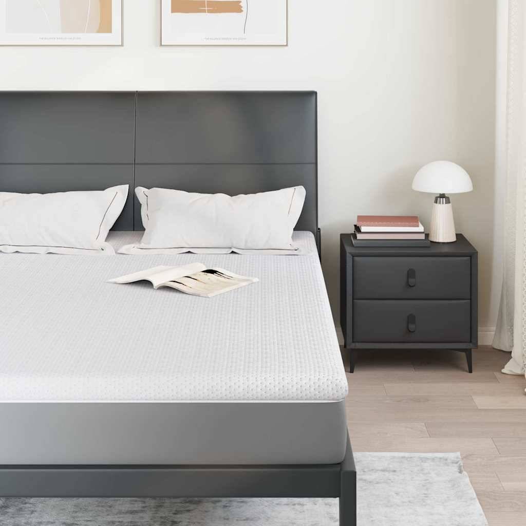 Ein Schlafzimmer präsentiert ein ordentlich gemachtes Doppelbett mit weißen Kissen und einem Nachttisch, auf dem Bücher und eine Lampe stehen, was einen minimalistischen Look erzeugt.