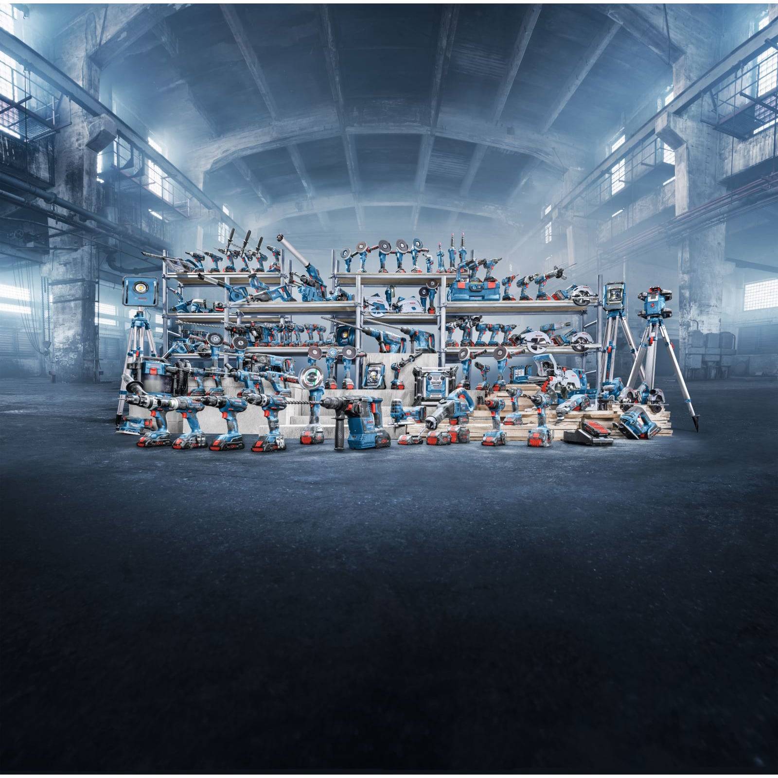 Ein Arrangement verschiedener Werkzeuge und Ausrüstungen, die auf mehreren Regalen in einem großen Industrielager mit hohen Decken und Fenstern angeordnet sind.