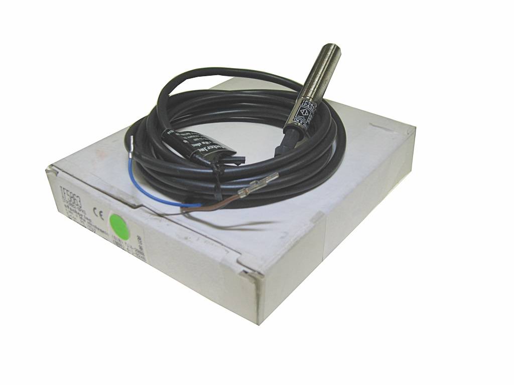 Metallischer zylindrischer Sensor mit aufgewickeltem Kabel, der auf einer weißen Schachtel liegt.