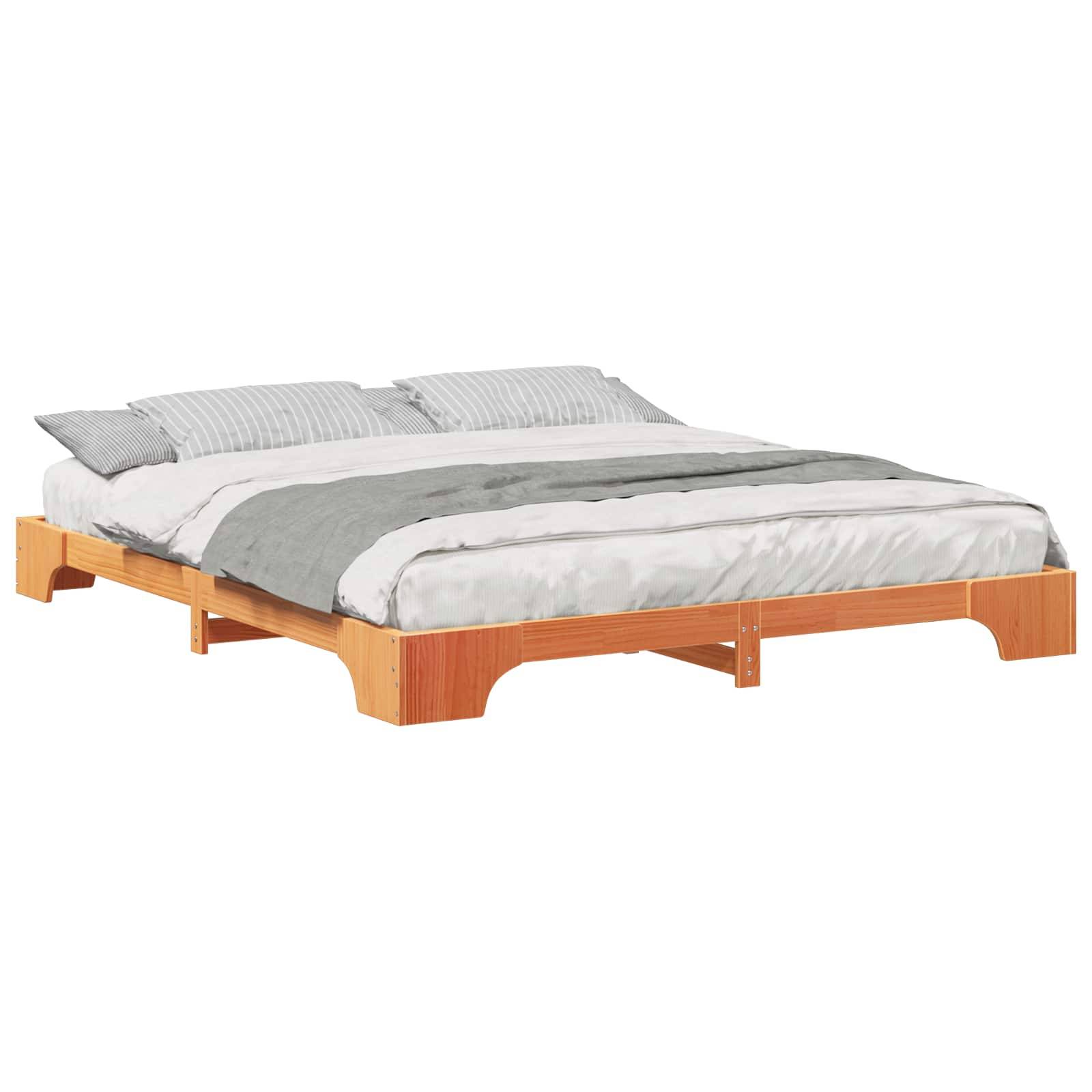 Ein minimalistisches Holz-Plattformbett mit einer weißen Matratze, einer grauen Decke und zwei gestreiften Kissen darauf.