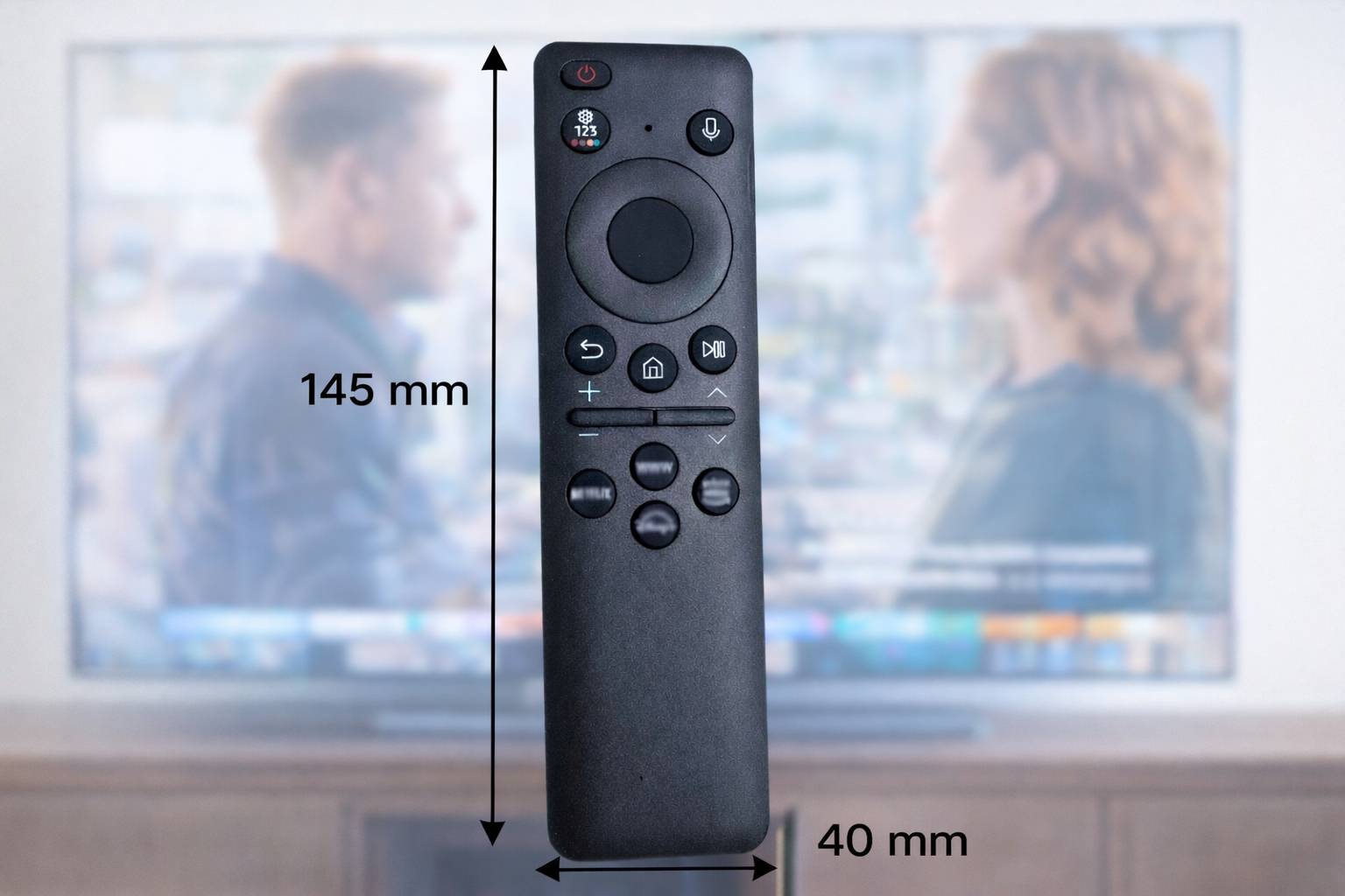 Eine Fernbedienung mit einer Höhe von 145 mm und einer Breite von 40 mm, gezeigt vor einem unscharfen Hintergrund mit zwei Personen, die auf einem Fernsehbildschirm miteinander sprechen.