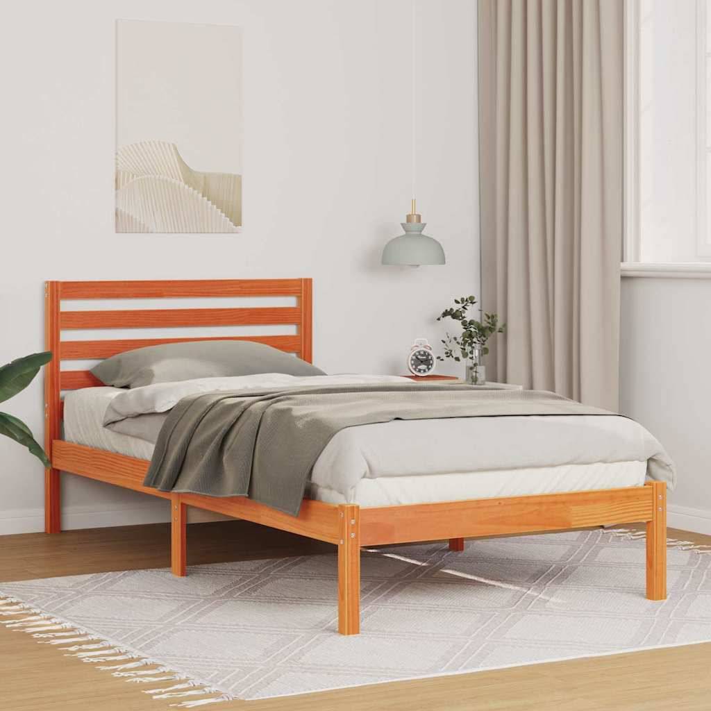 Ein Holzbett mit grauer Bettwäsche und Kissen steht in einem Schlafzimmer. Eine kleine Pflanze und eine Lampe befinden sich neben dem Bett, und an der Wand hängt ein gerahmtes Kunstwerk.