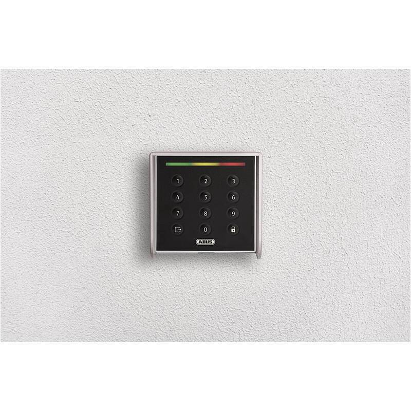 Wandmontiertes ABUS-Tastenfeld für die Zutrittskontrolle an einer einfachen, hellen Wand, mit beleuchtetem Statusbalken und Nummerntasten.
