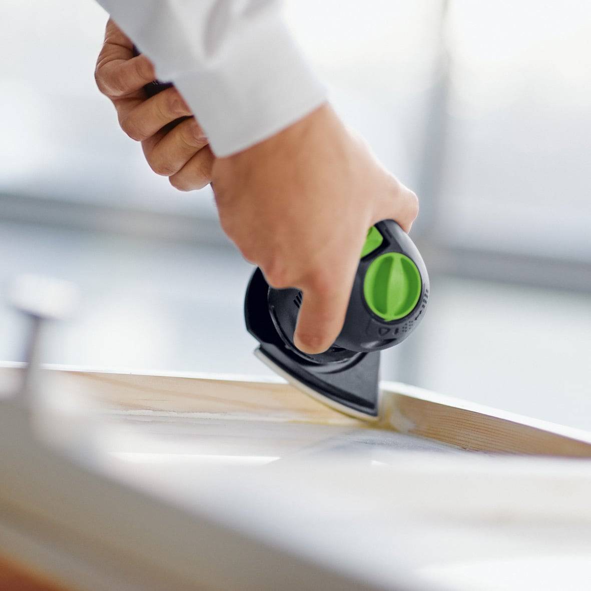 Hand hält ein Bügeleisen, drückt die Kante einer Holzoberfläche, was auf eine Aufgabe im Zusammenhang mit Tischlerei oder Möbelherstellung hindeutet.