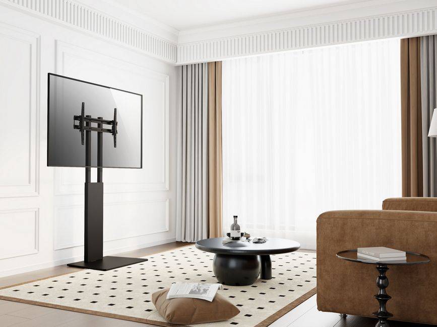 Modernes Wohnzimmer mit an der Wand montiertem Fernseher, schwarzem Medienregal, rundem Couchtisch, braunem Sofa und großen transparenten Vorhängen über hellen Fenstern.