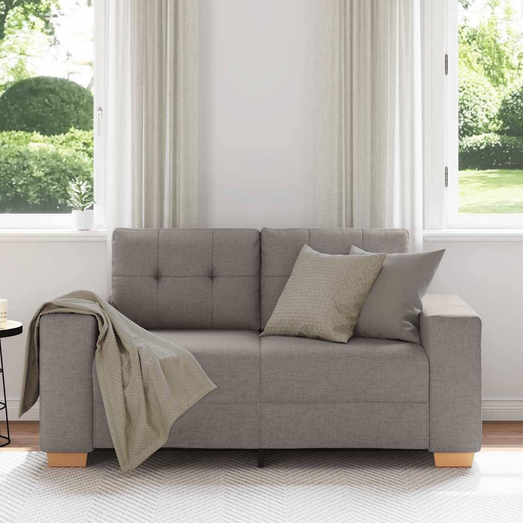 Ein modernes Wohnzimmer mit einem grauen Sofa, grauen und beigefarbenen Kissen, einer Decke, einem runden Beistelltisch mit einer schwarzen Lampe und großen Fenstern.