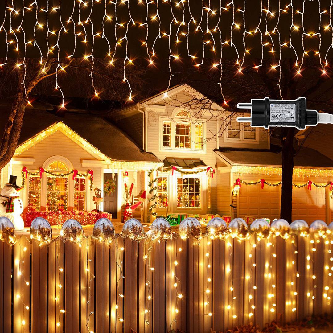 Haus, das nachts mit warmweißen Weihnachtslichtern und Girlanden dekoriert ist, mit einem Steckverbinder im Vordergrund.