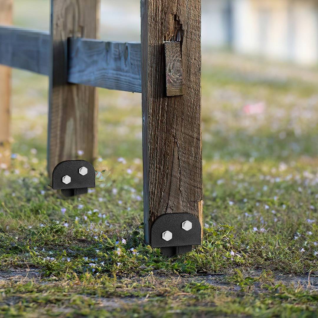 Nahaufnahme von zwei verwitterten Holzzaunpfählen mit schwarzen Metallklammern an der Basis, die auf grasbewachsenem Boden stehen.