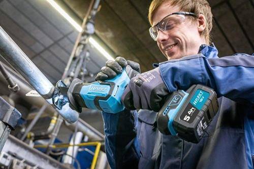 Eine Person mit Schutzbrille und Handschuhen verwendet ein Elektrowerkzeug an Metallrohren in einer industriellen Umgebung und konzentriert sich dabei sehr konzentriert.