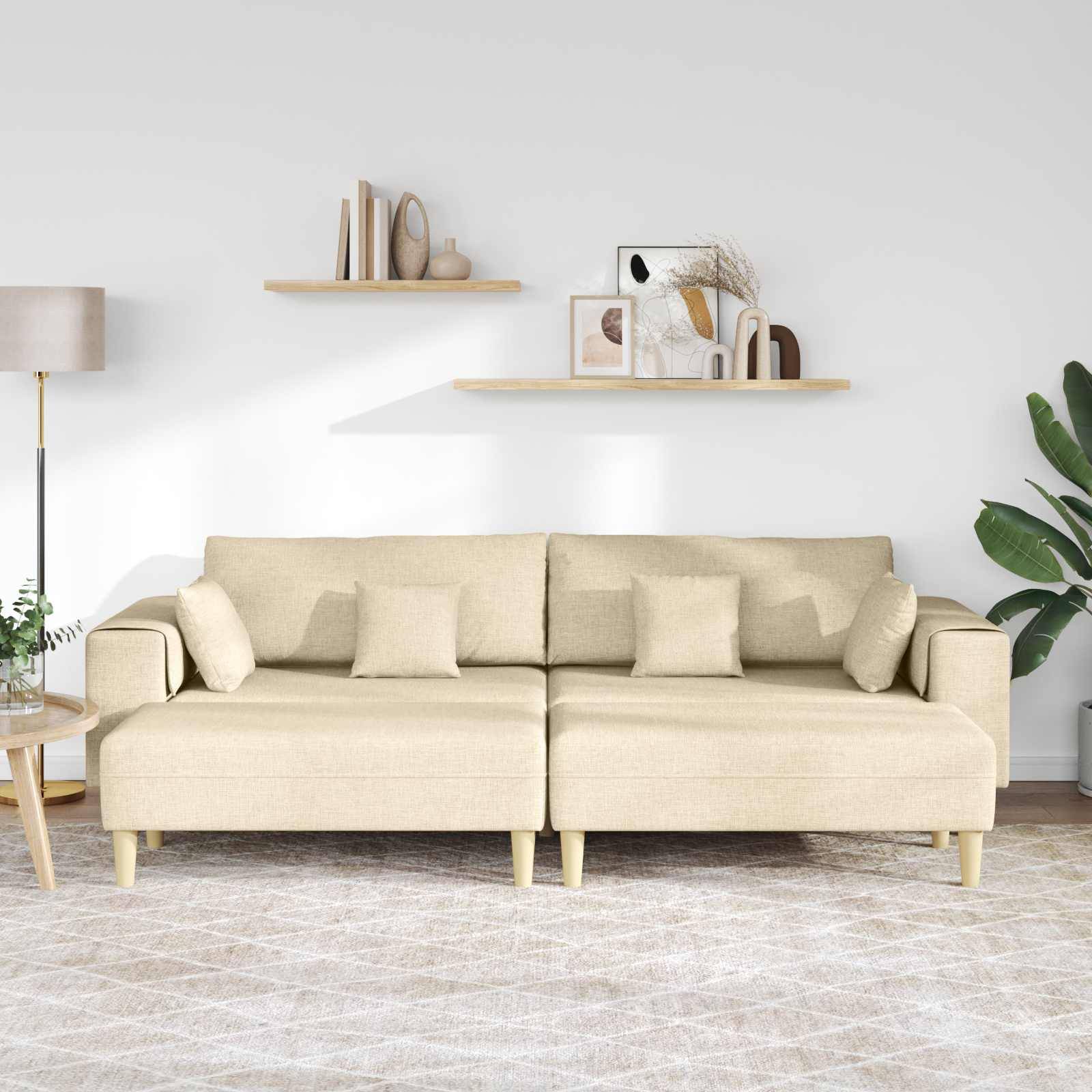 Ein beige Sofa mit mehreren Kissen steht in einem Wohnzimmer. Eine Stehlampe, zwei Wandregale mit Dekoration und eine Pflanze befinden sich im Hintergrund.