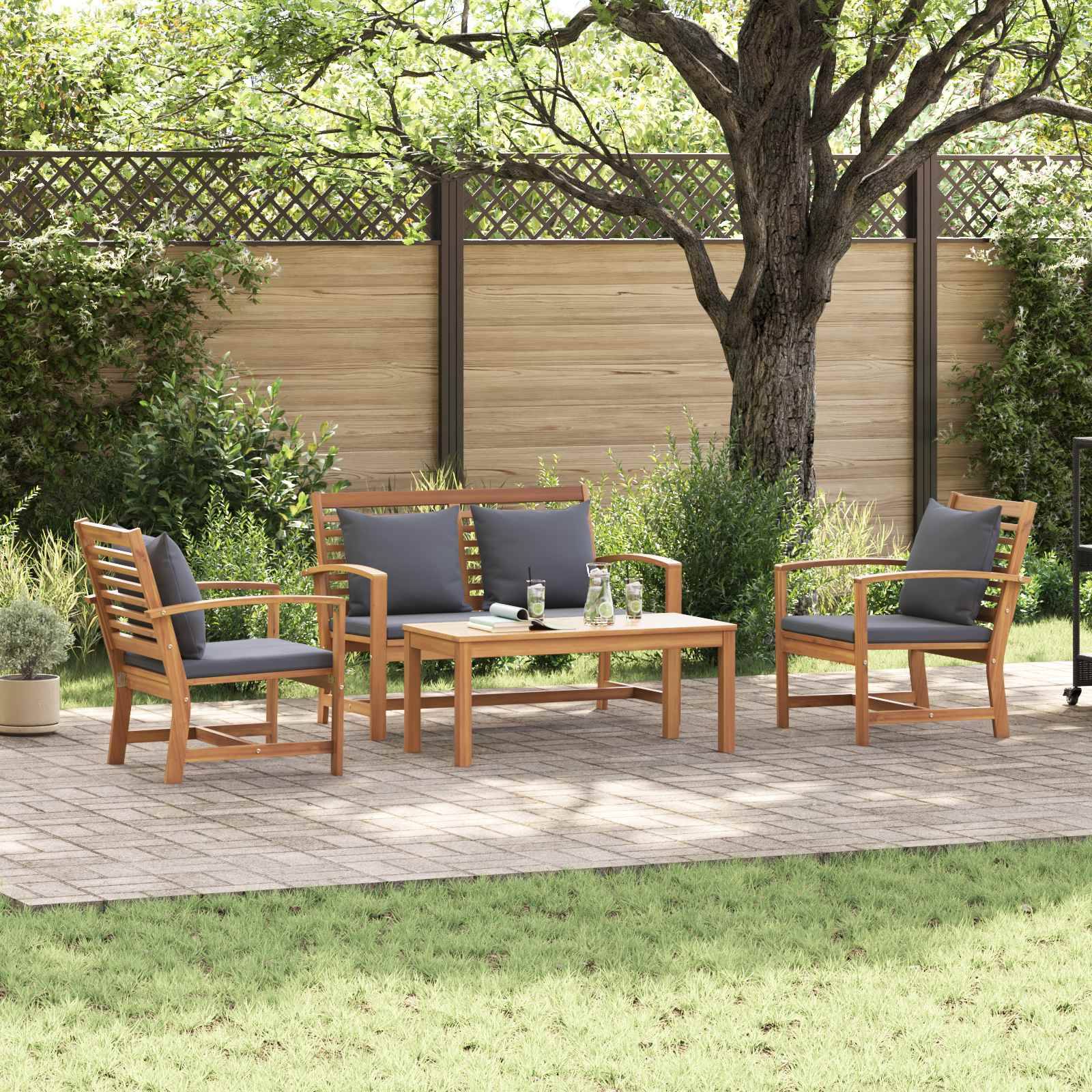 Outdoor-Gartenmöbel-Set mit Holzstühlen und einem Tisch auf einer gefliesten Oberfläche, umgeben von Grünpflanzen und einem Baum, angrenzend an einen Holzzaun.