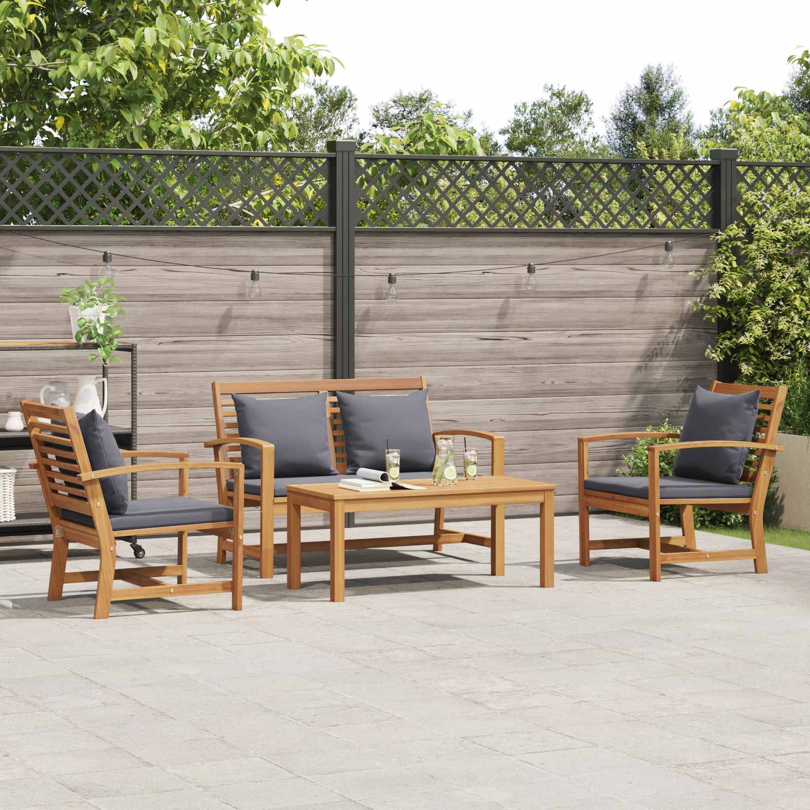 Gartenmöbel-Set im Freien mit vier gepolsterten Stühlen und einem Holztisch auf einer Steinoberfläche, umgeben von einem Holzzaun und Grünflächn.