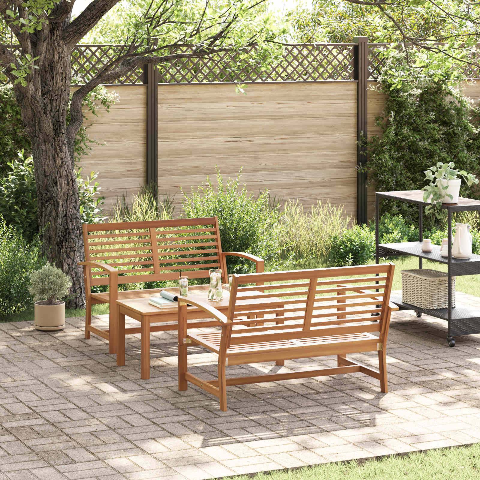 Eine Terrasse im Garten mit Holzbänken und einem Tisch unter einem Baum. Topfpflanzen schmücken den steingepflasterten Bereich und sorgen für eine ruhige Atmosphäre.