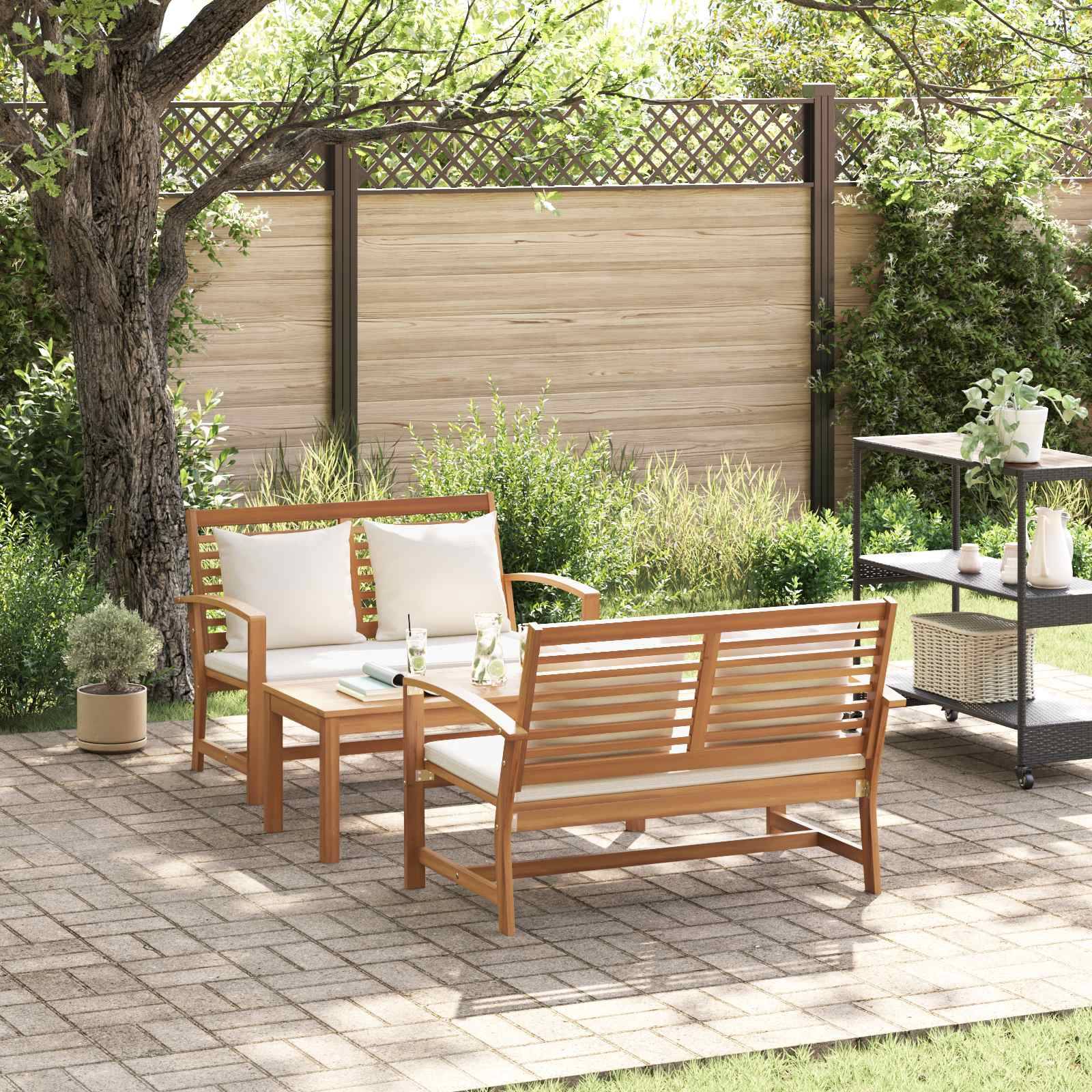 Holz-Outdoor-Sitzgarnitur mit beigen Kissen auf einer gepflasterten Terrasse, umgeben von Grünpflanzen. Ein kleiner Wagen steht in der Nähe und trägt Pflanzen und Dekorationsgegenstände.