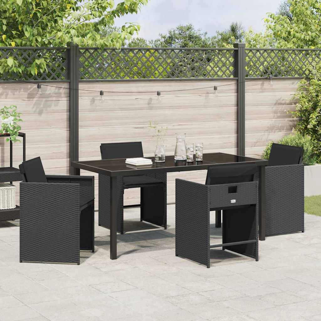 Outdoor-Terrasseneinrichtung mit einem schwarzen Tisch und sechs schwarzen Flechtgartenstühlen, einem grauen Zaun mit Grünpflanzen oben und einem Pflanzer in der Ecke.