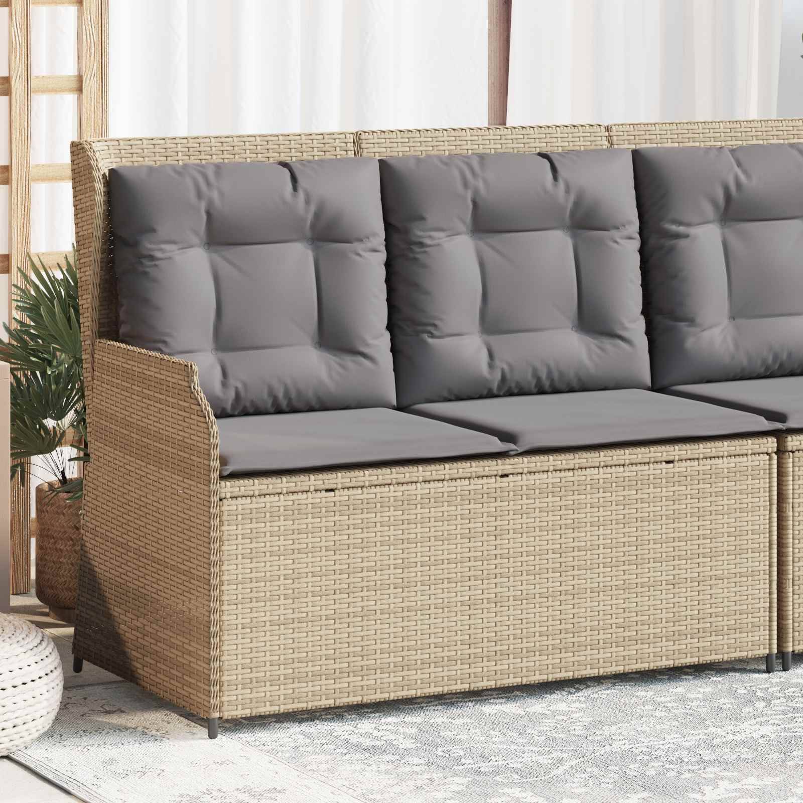 Outdoor-Rattansofa mit drei grauen gepolsterten Sitzen, vor einem leicht drapiertem Hintergrund. Eine Topfpflanze ist seitlich sichtbar.