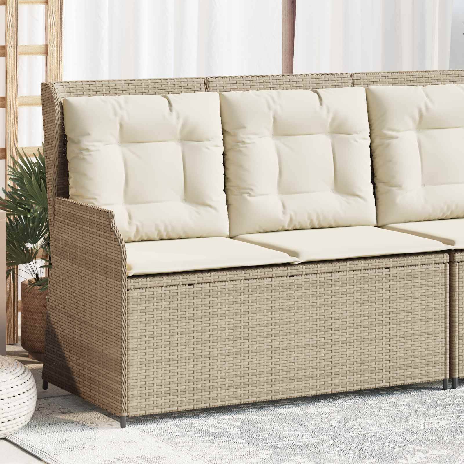 Eine beige geflochtene Outdoor-Couch mit cremefarbenen Kissen, platziert auf einem hellgemusterten Teppich, neben einer Topfpflanze unter weichem, natürlichem Licht.