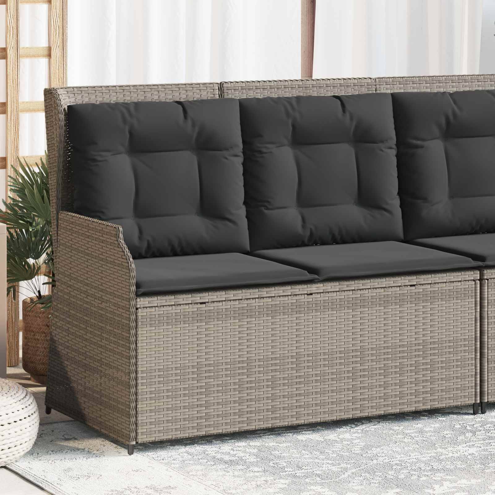 Eine Rattanstil-Outdoor-Couch mit dunklen gepolsterten Sitzen und Rückenlehnen steht auf einem hellgefärbten Teppich, mit Topfpflanzen in der Nähe.